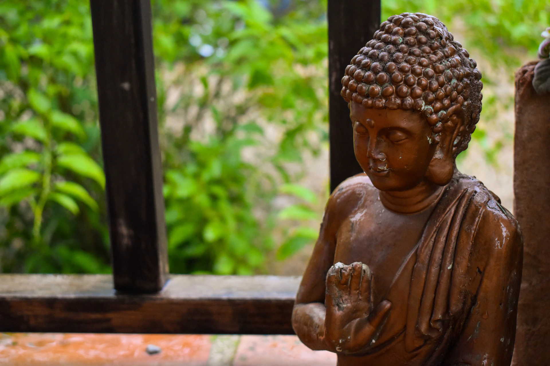 A small buddha statue sits outdoors near greenery.