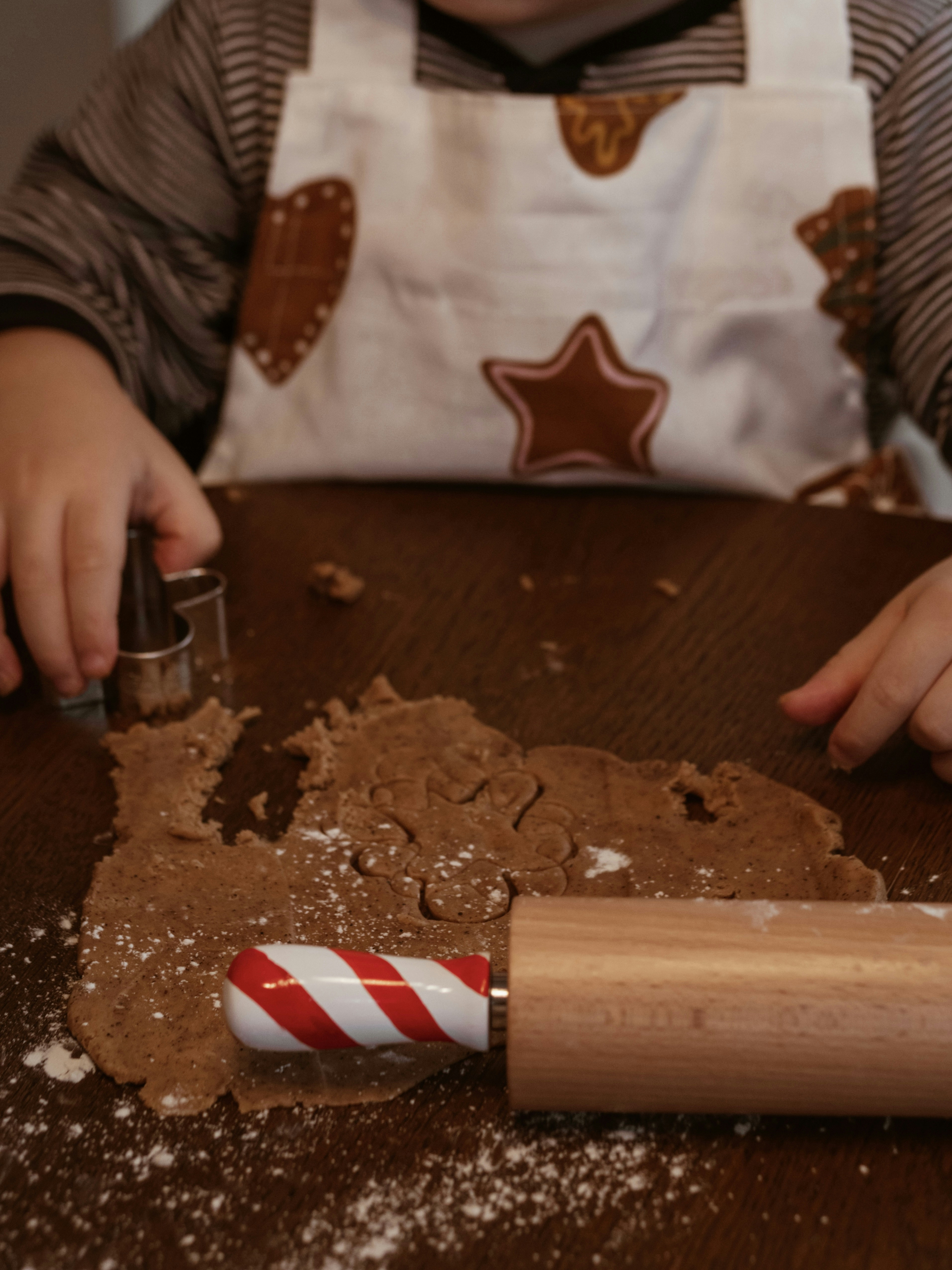 Child cutting gingerbread dough with cookie cutters.