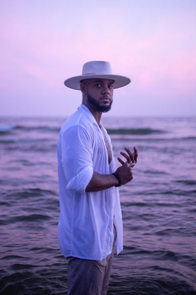 Man in hat and white shirt by the ocean.