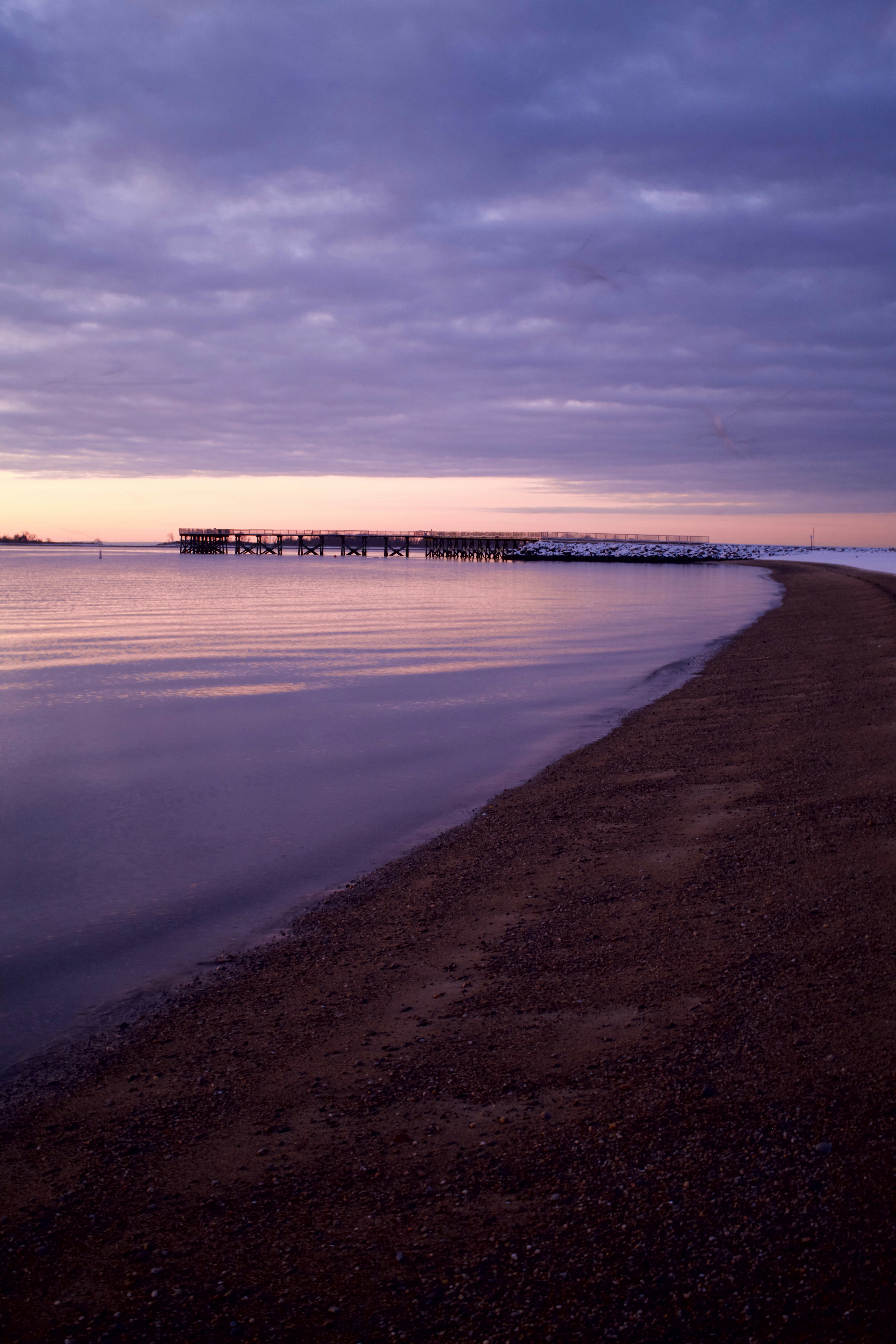 Purple sunset over a calm ocean with a pier.