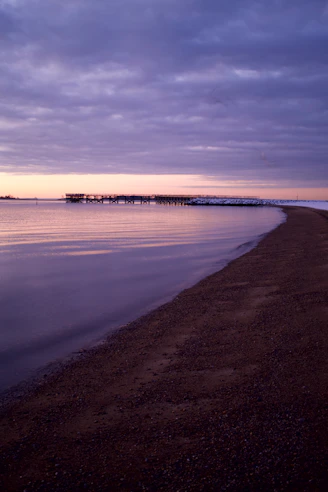 Purple sunset over a calm ocean with a pier.