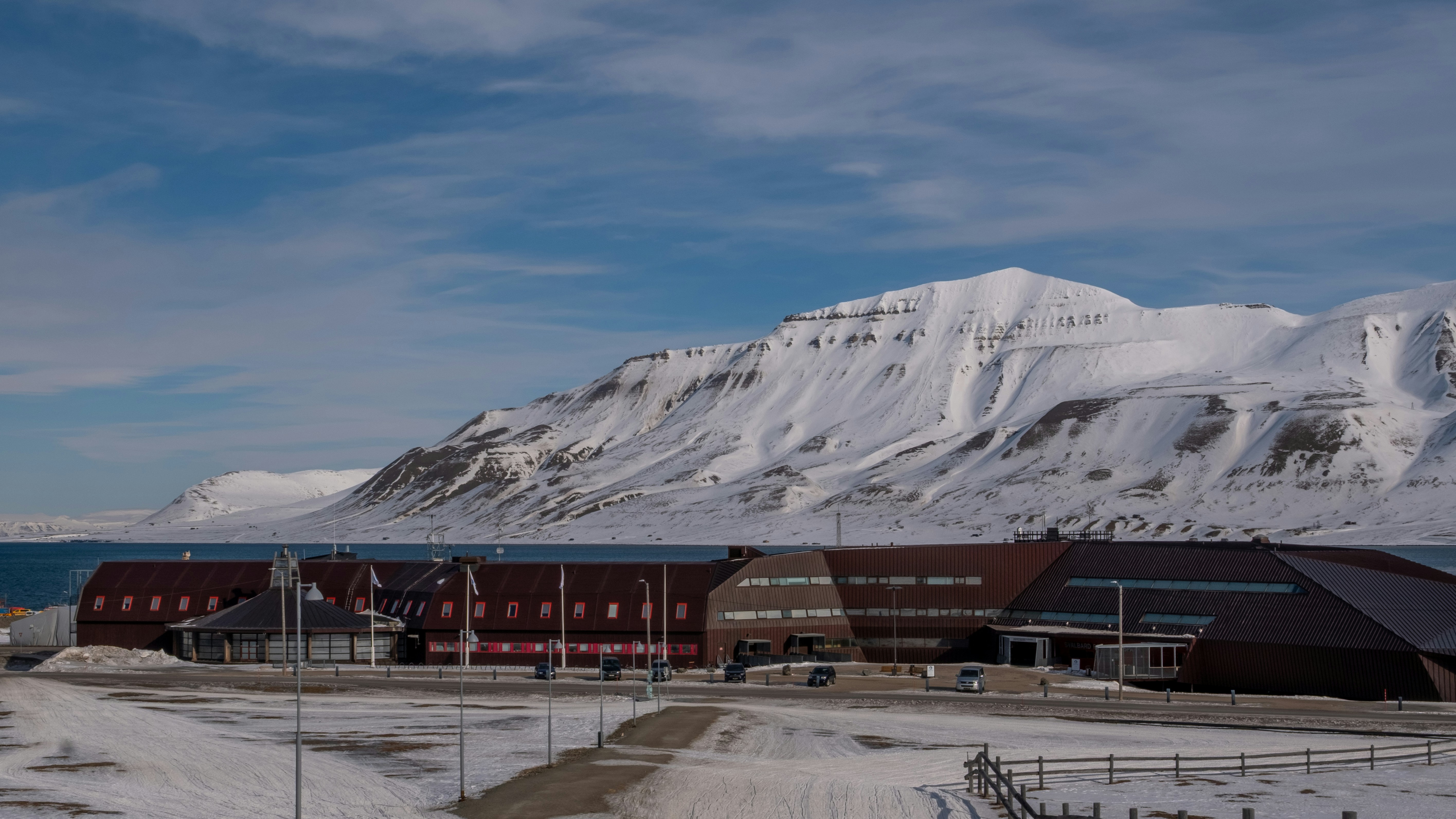 Snow-covered mountains overlook buildings by the sea.