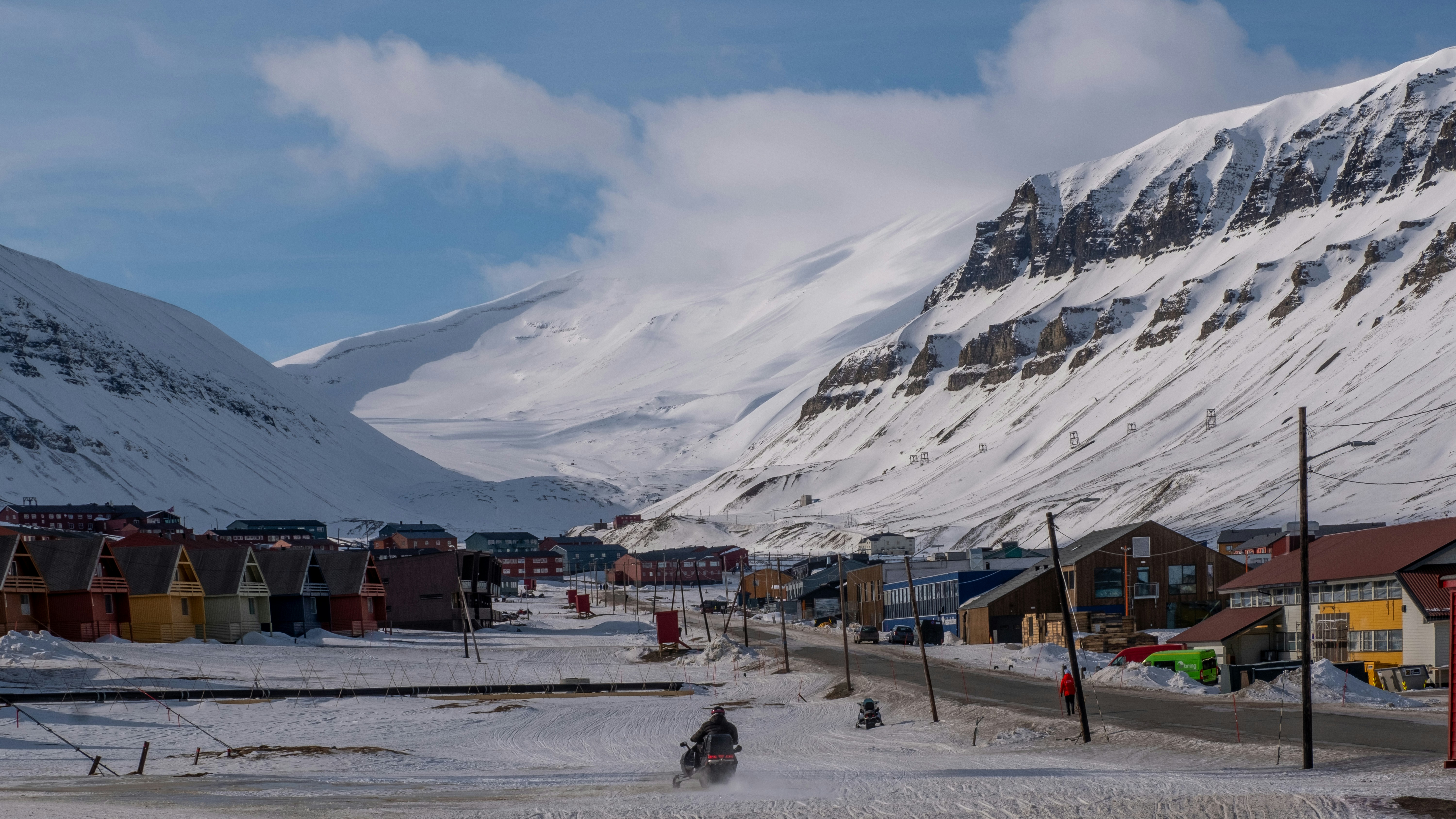 Snowy village nestled between snow-capped mountains under a cloudy sky.