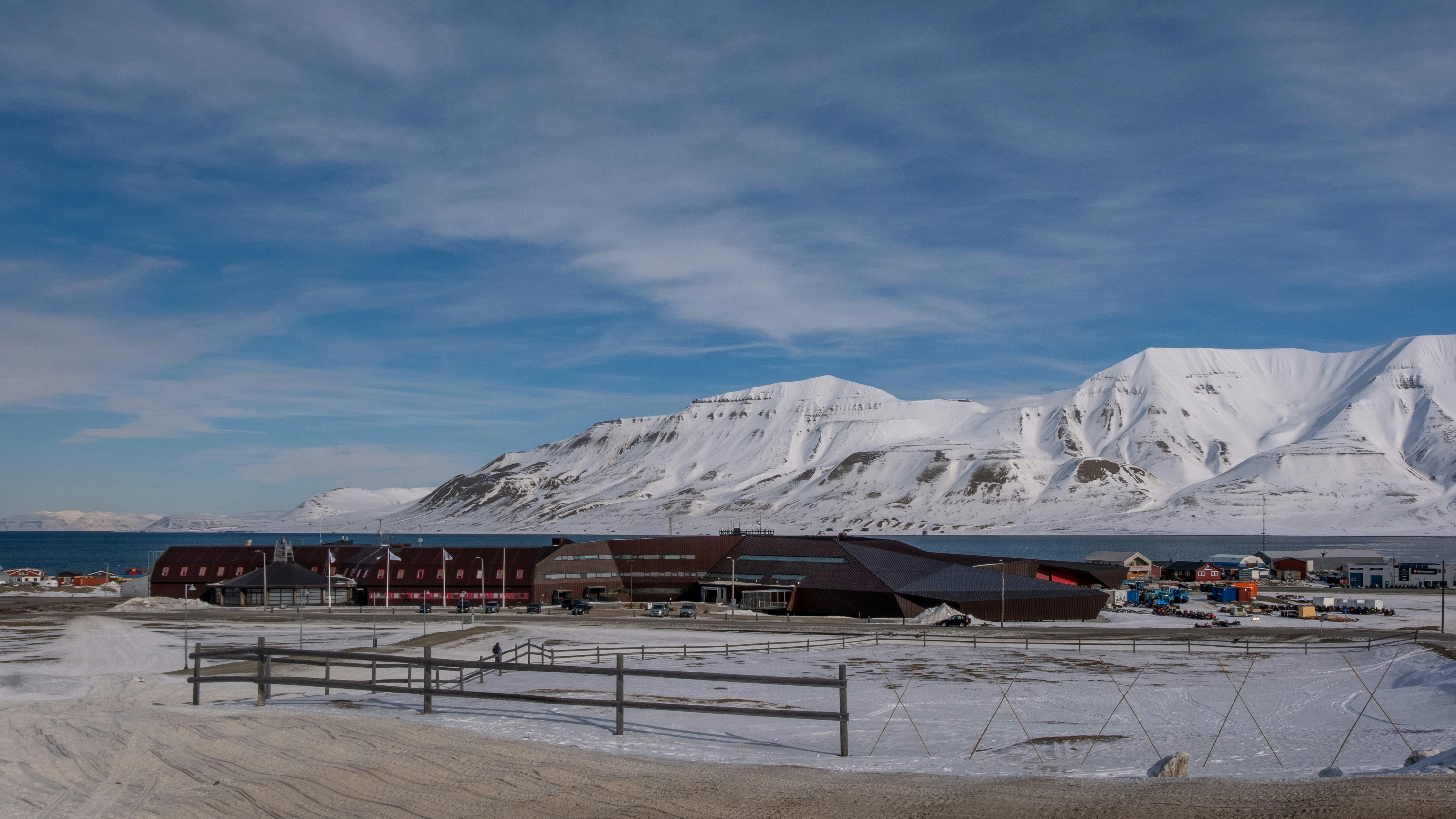Snowy village with mountains and ocean under blue sky.