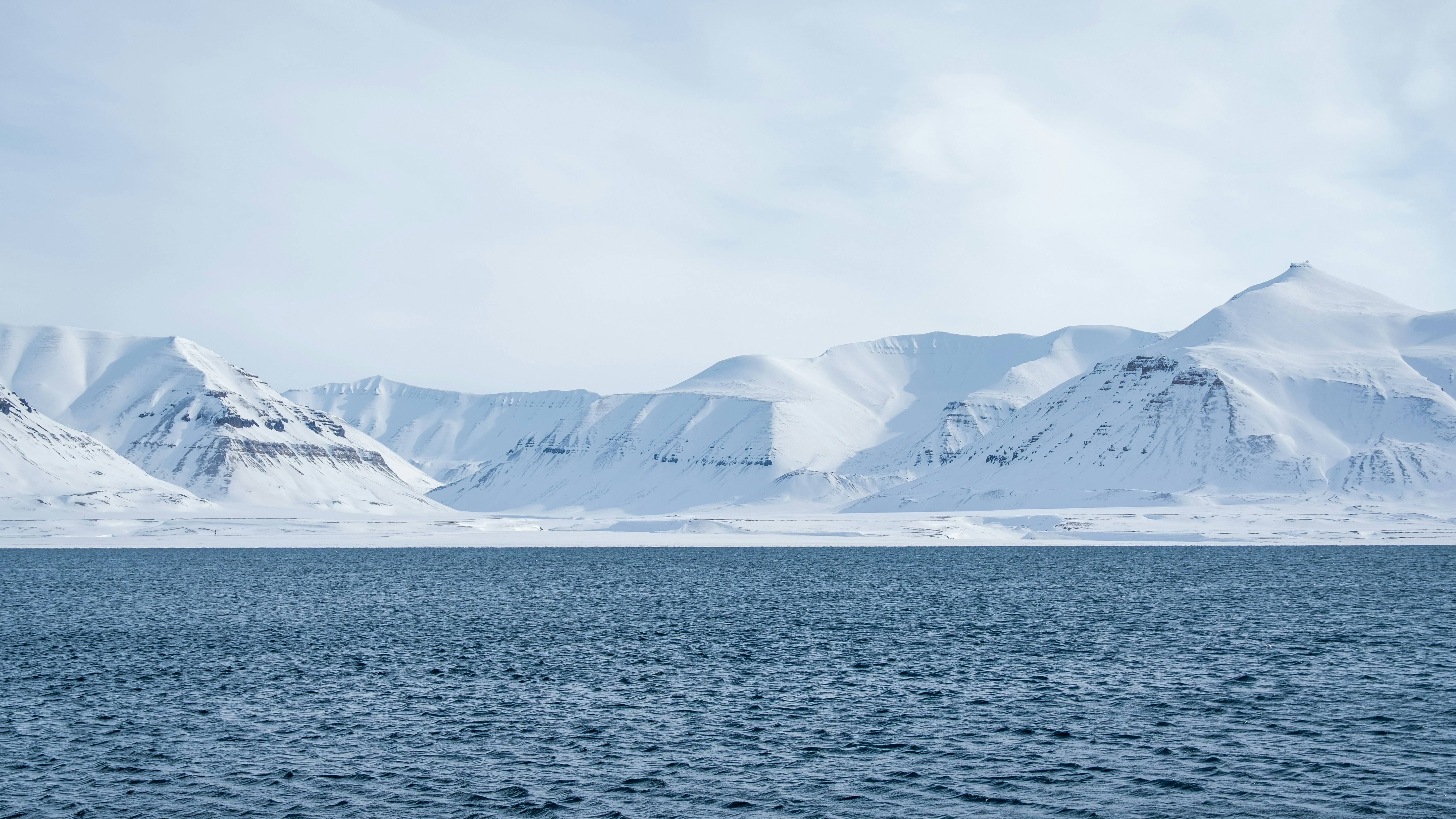 Snow-covered mountains rise above a calm blue sea.