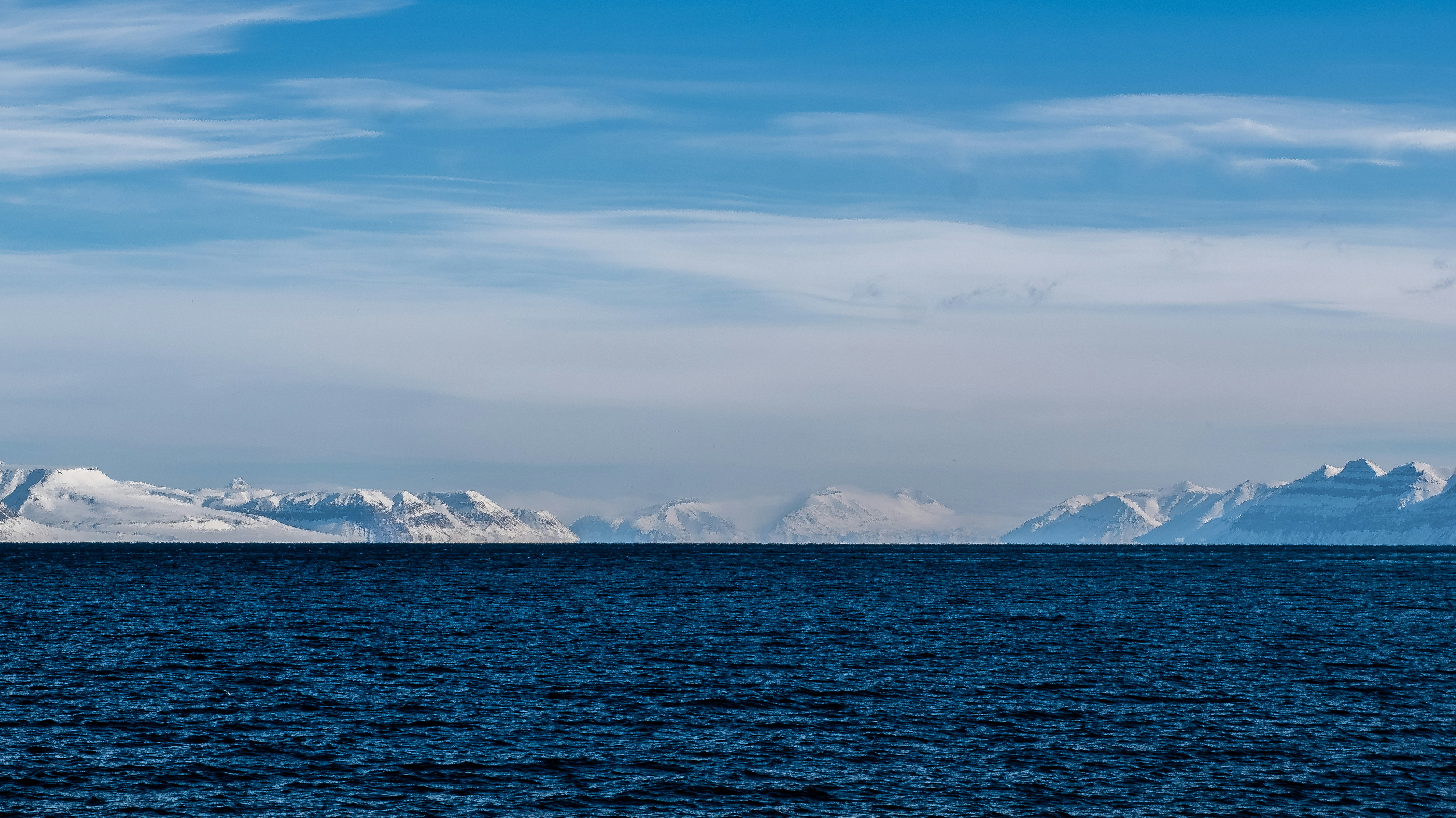 Blue ocean water with snow-capped mountains in distance.