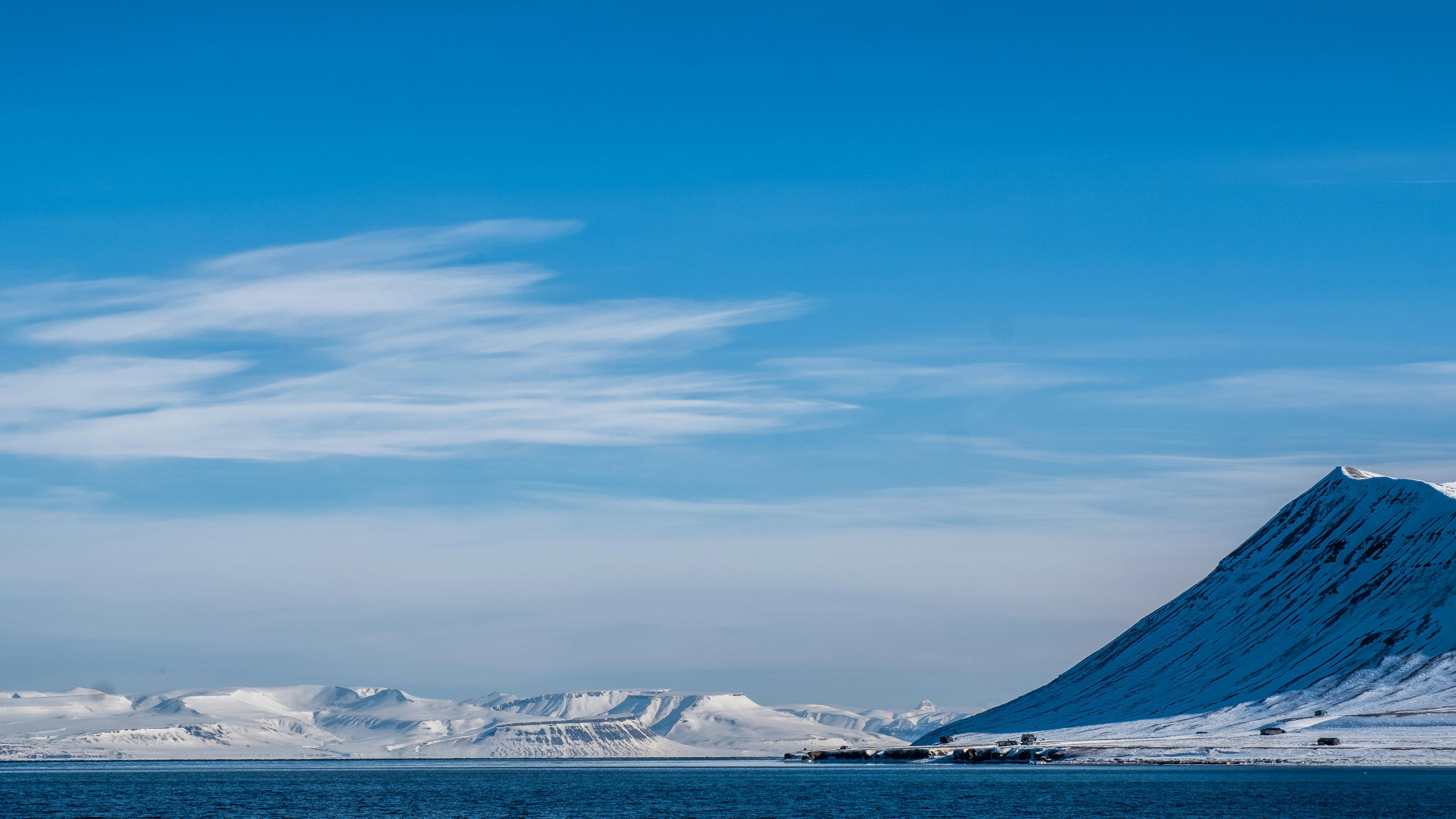 Snowy mountains meet the ocean under a clear blue sky.