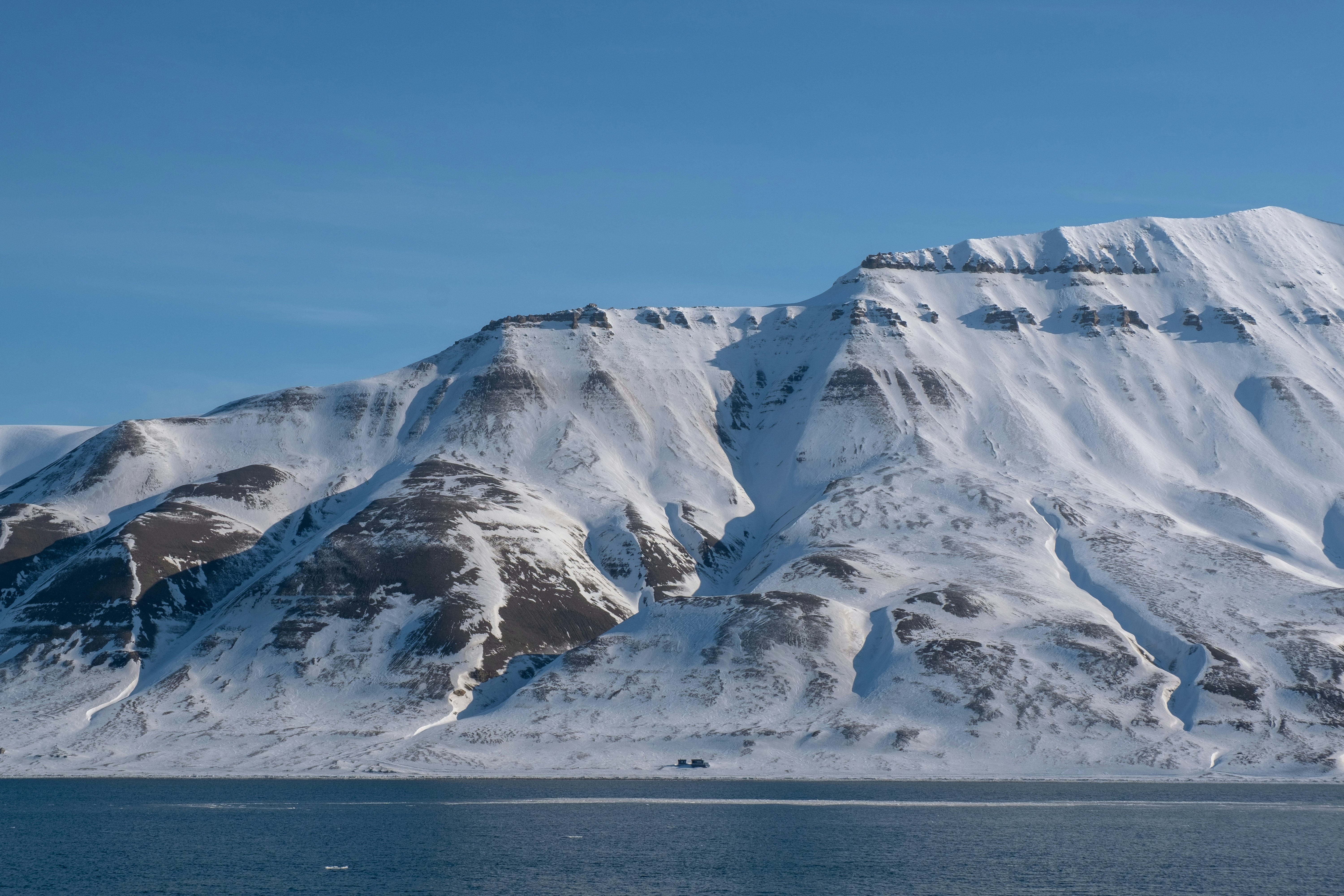 Snow-covered mountains rise above a calm blue sea