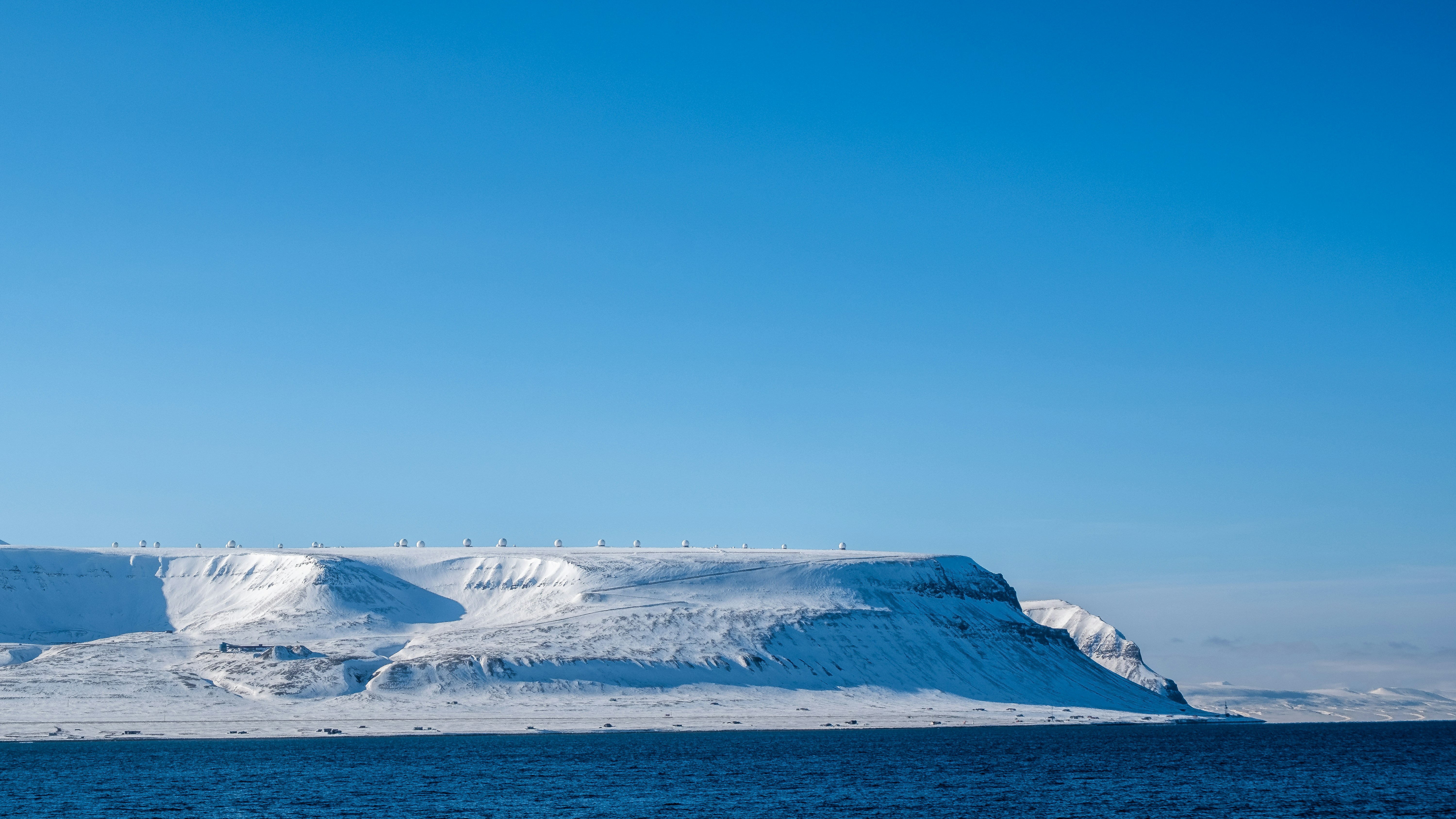 Snow covered mountains and blue ocean under clear sky
