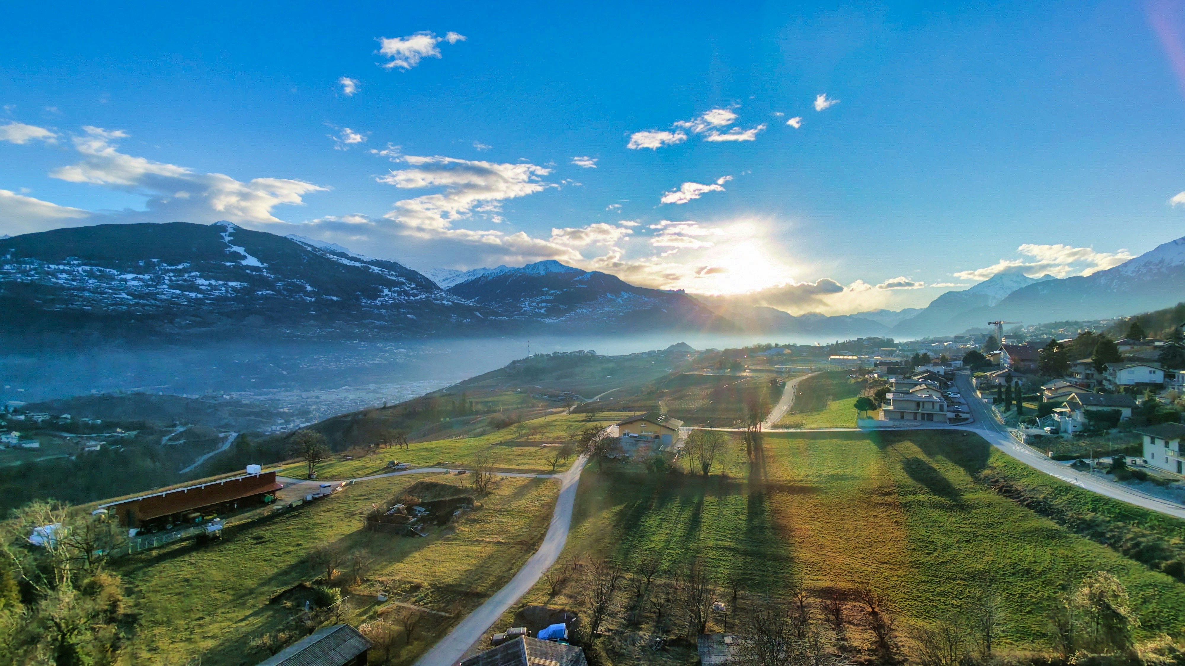 Sun shines over a valley with mountains and village.