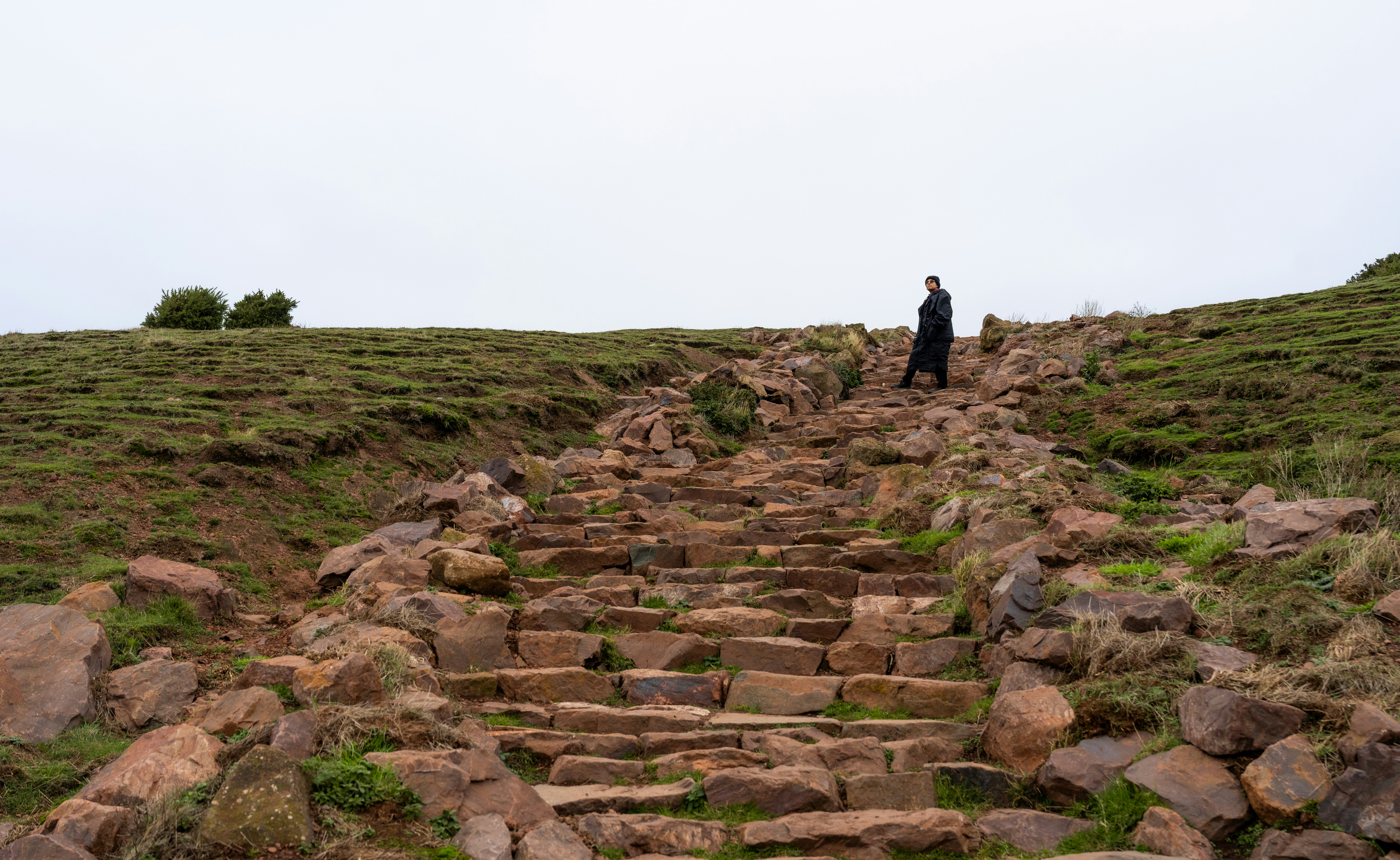 Person walks up ancient stone steps on grassy hill.
