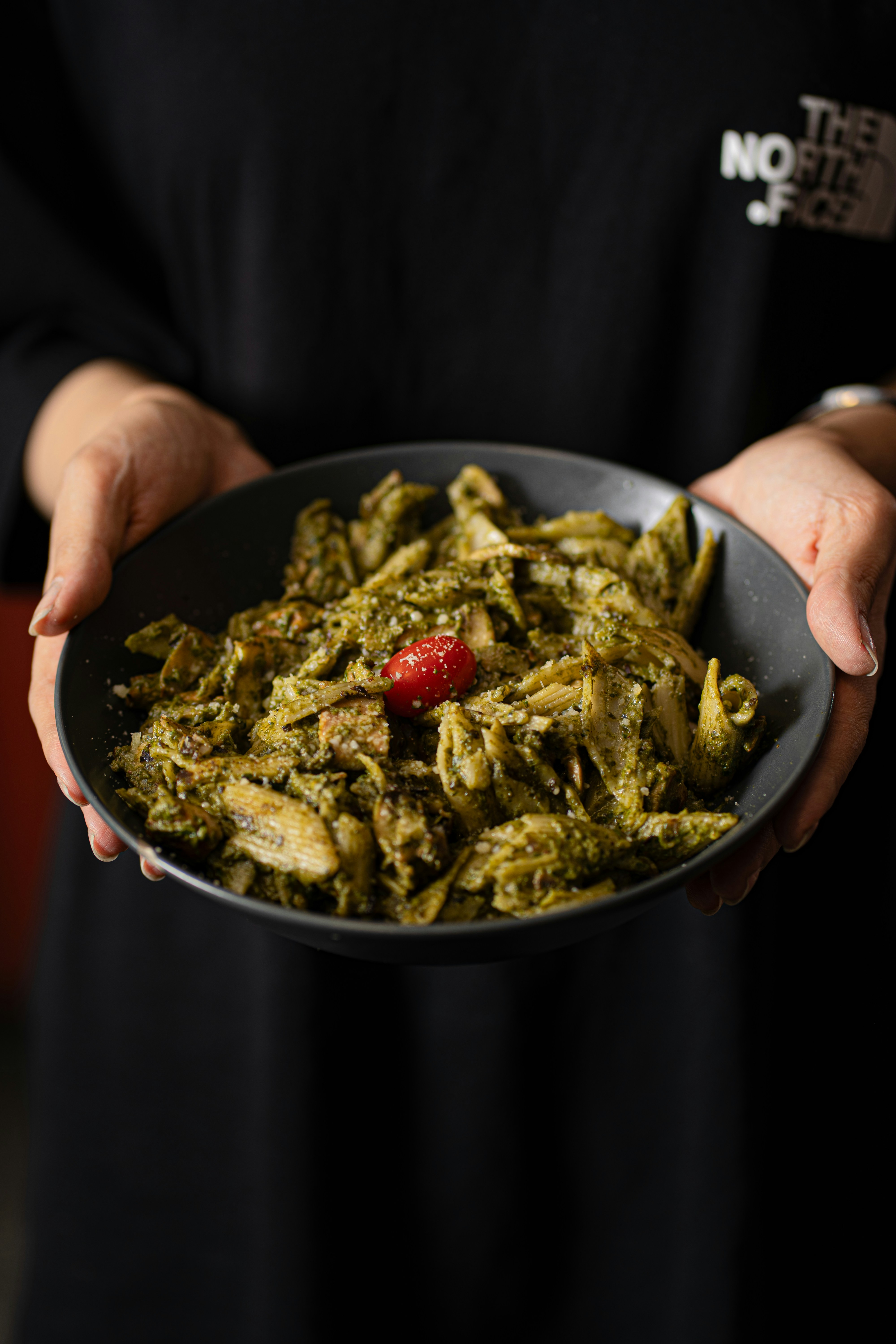 Uma tigela de macarrão penne com molho pesto e tomate.