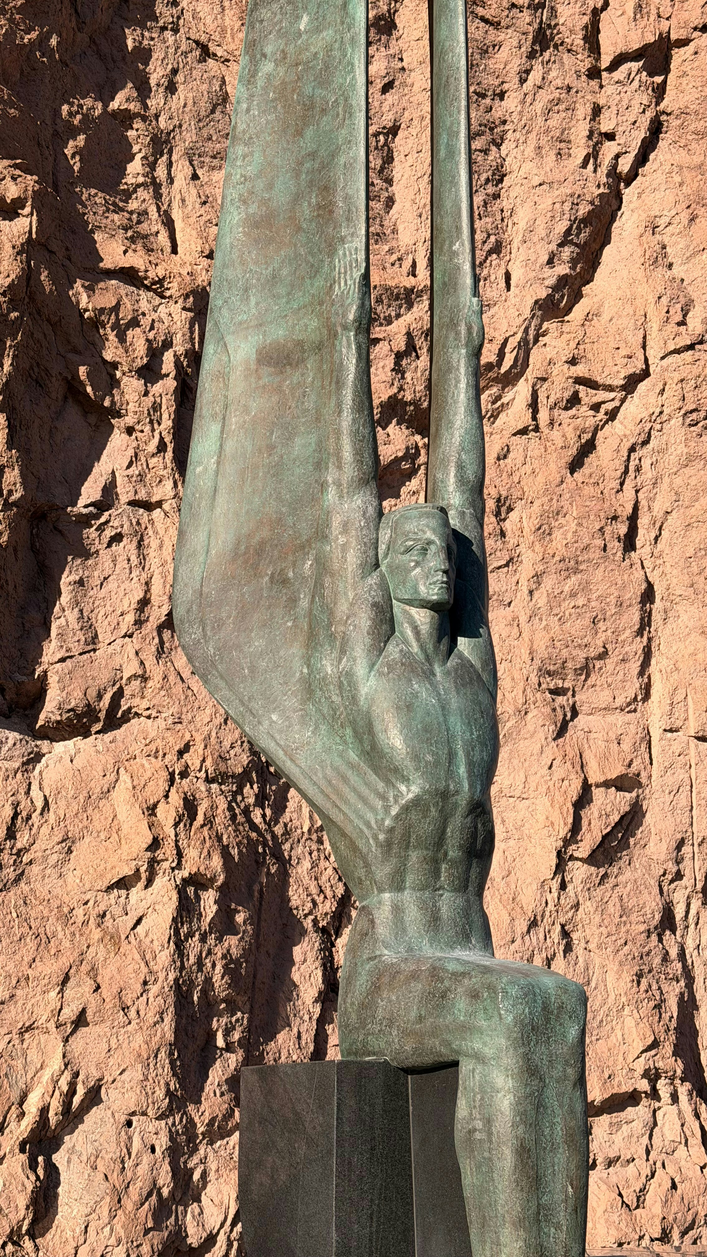 Bronze statue of a man with wings against rock wall