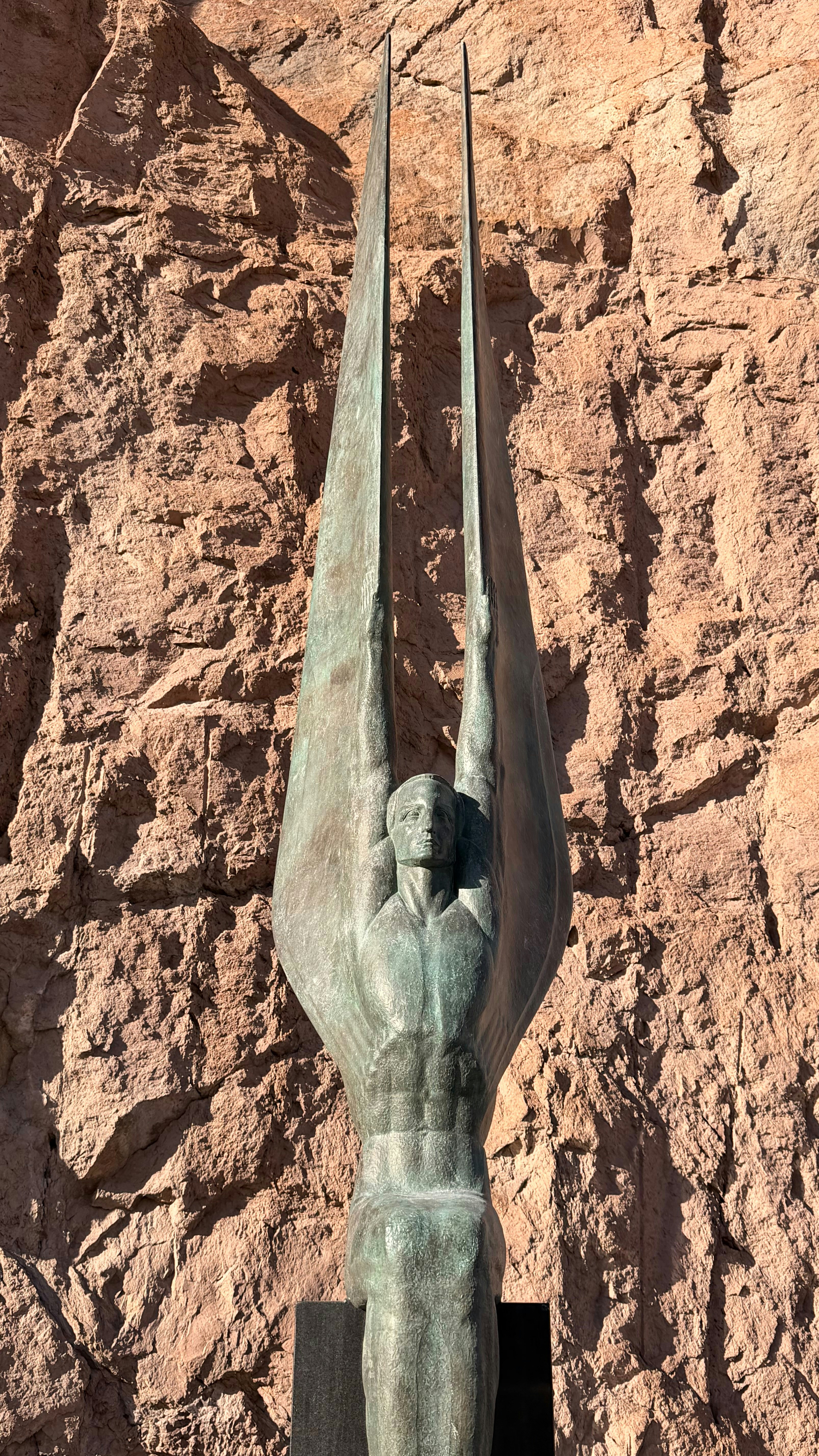 Bronze statue of a winged figure against rock wall