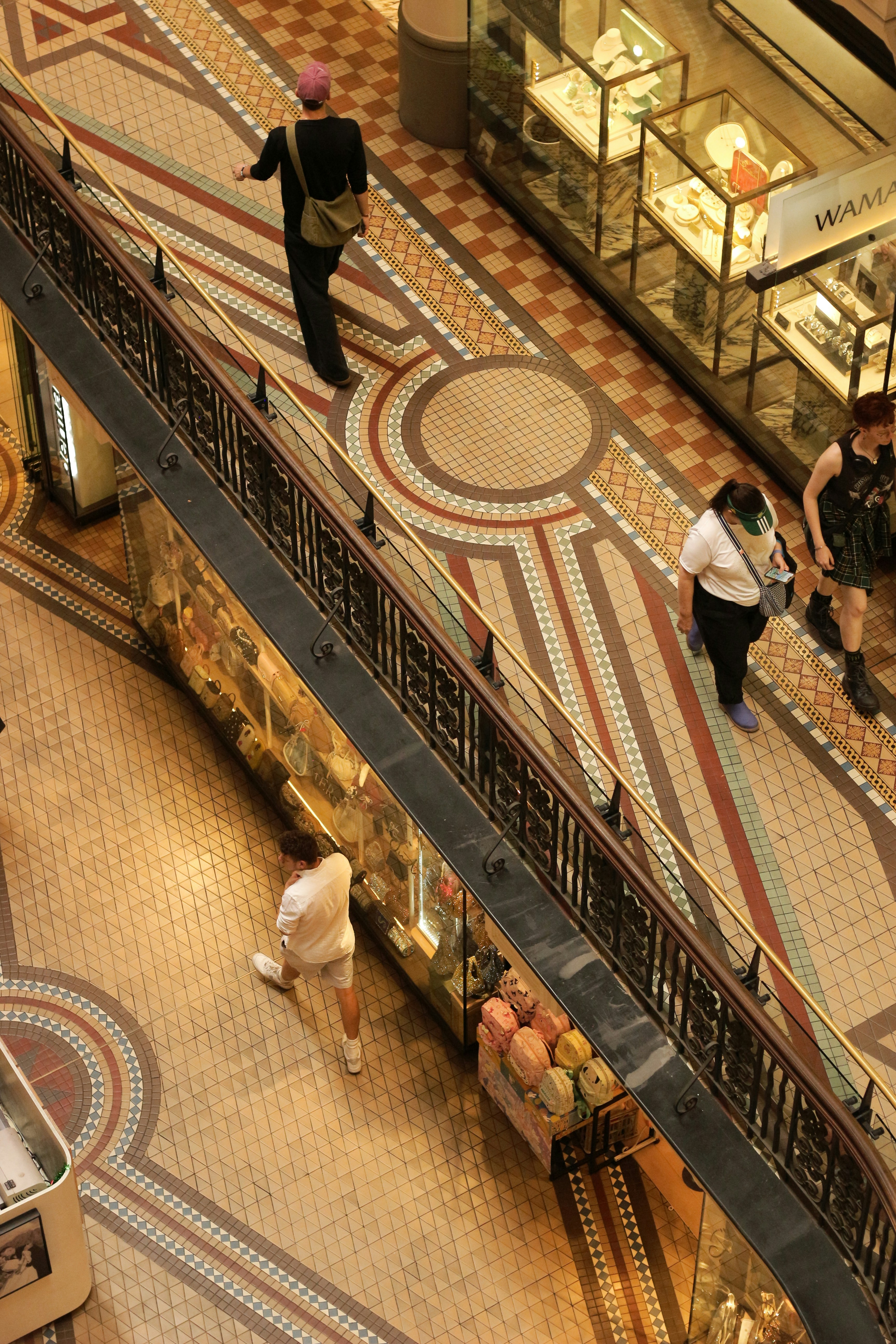 People walking on ornate tiled floor in a shopping arcade.