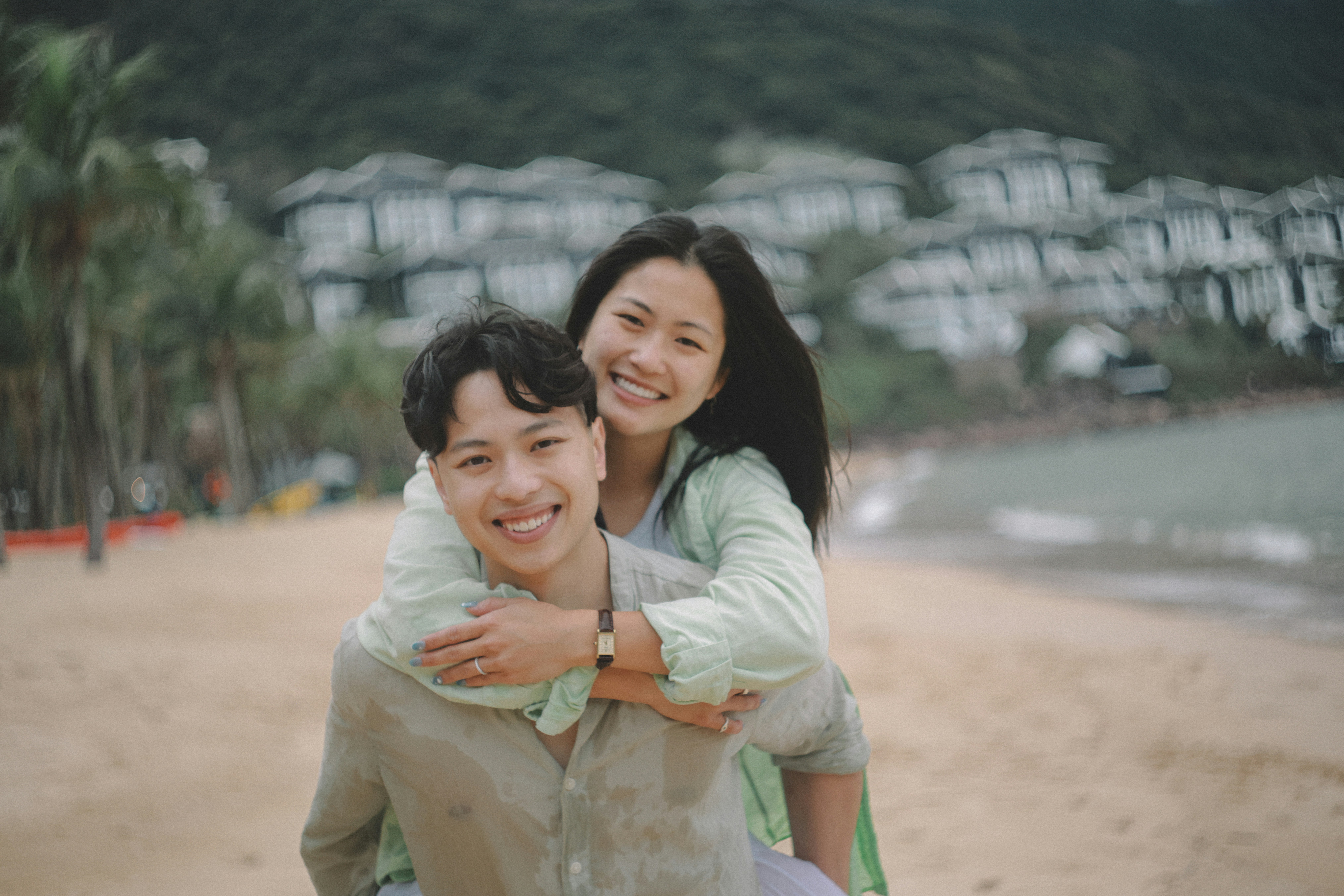 Couple smiling on a beach with buildings behind them