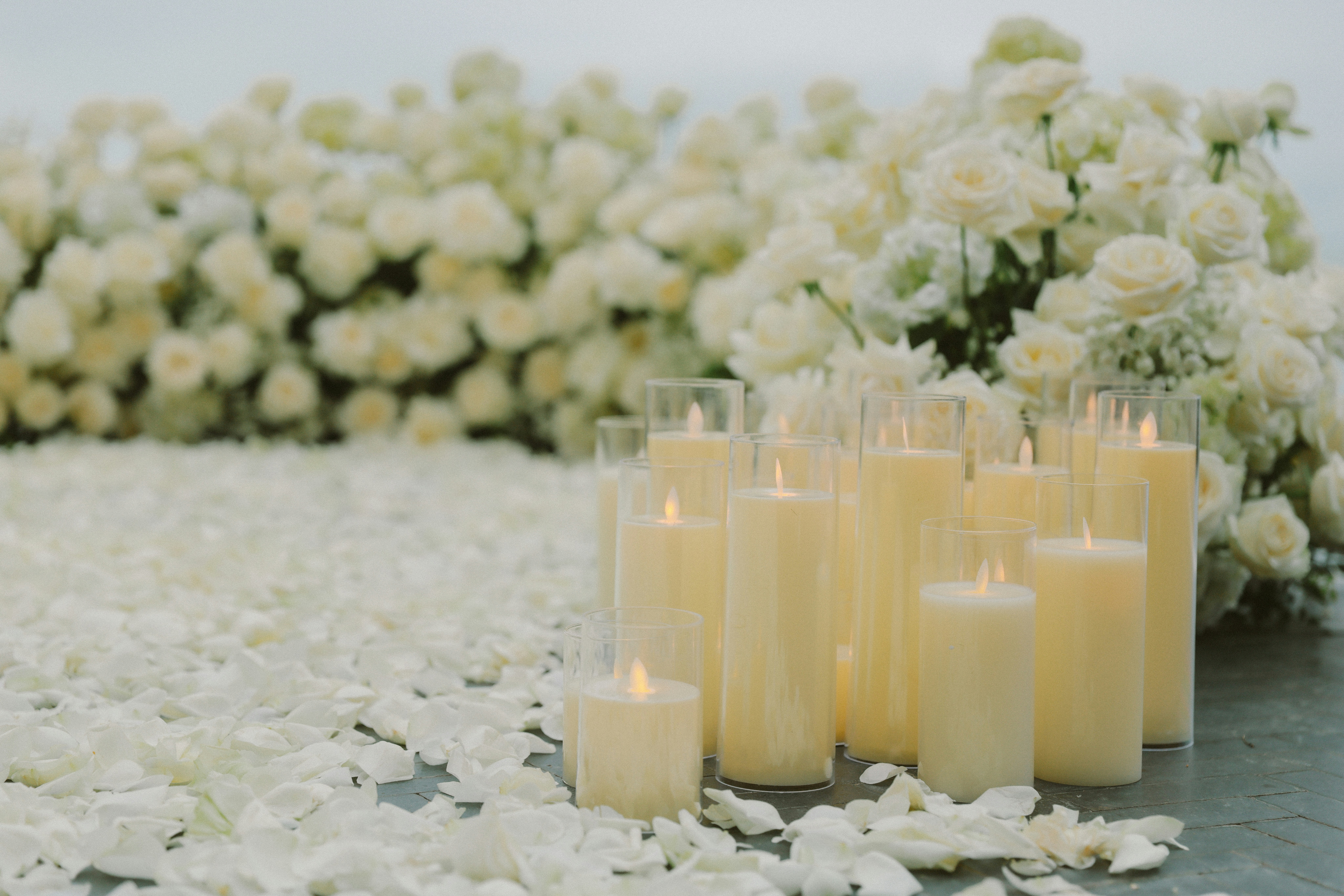 Lit candles surrounded by white rose petals and flowers