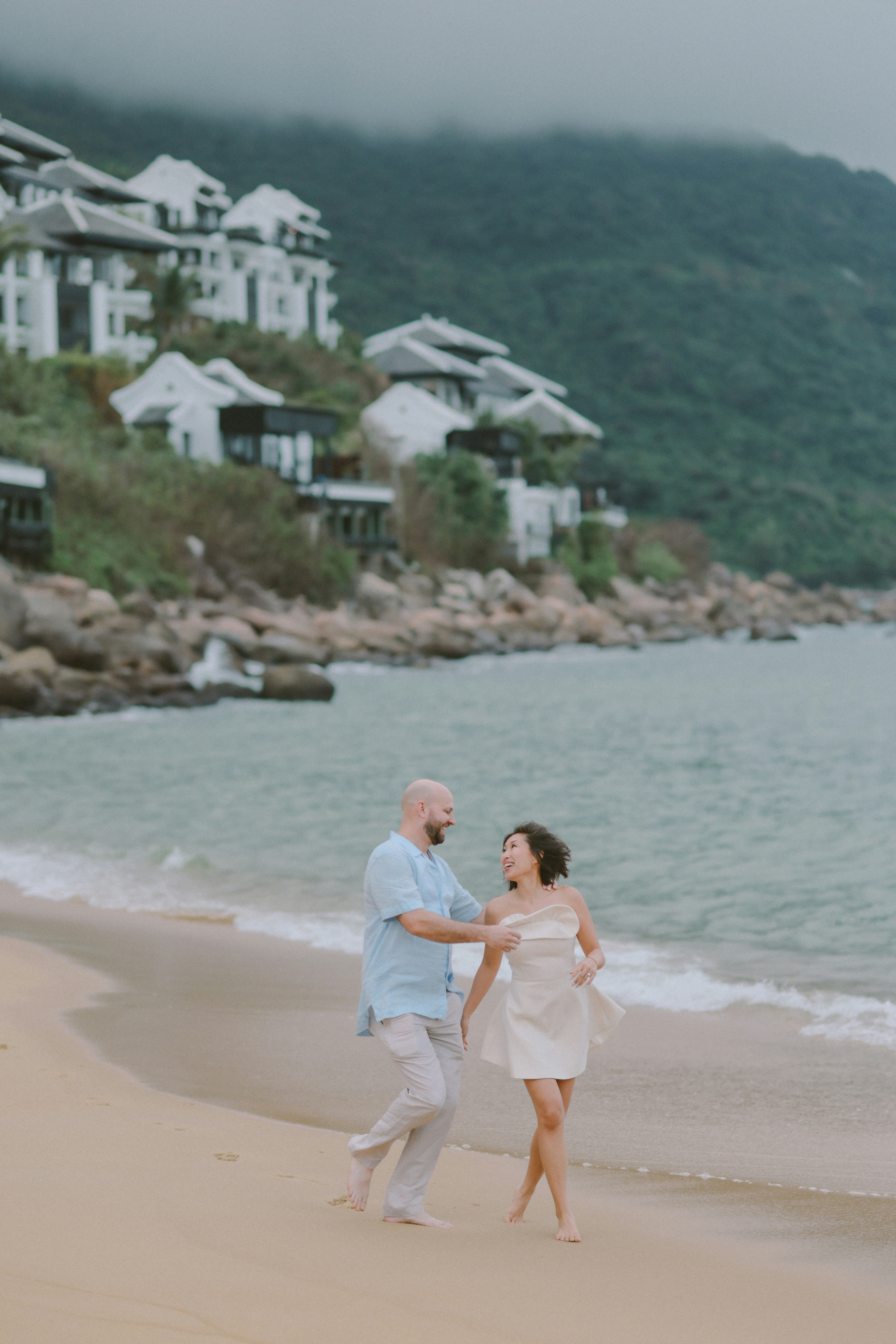 Couple walking on a sandy beach near ocean.