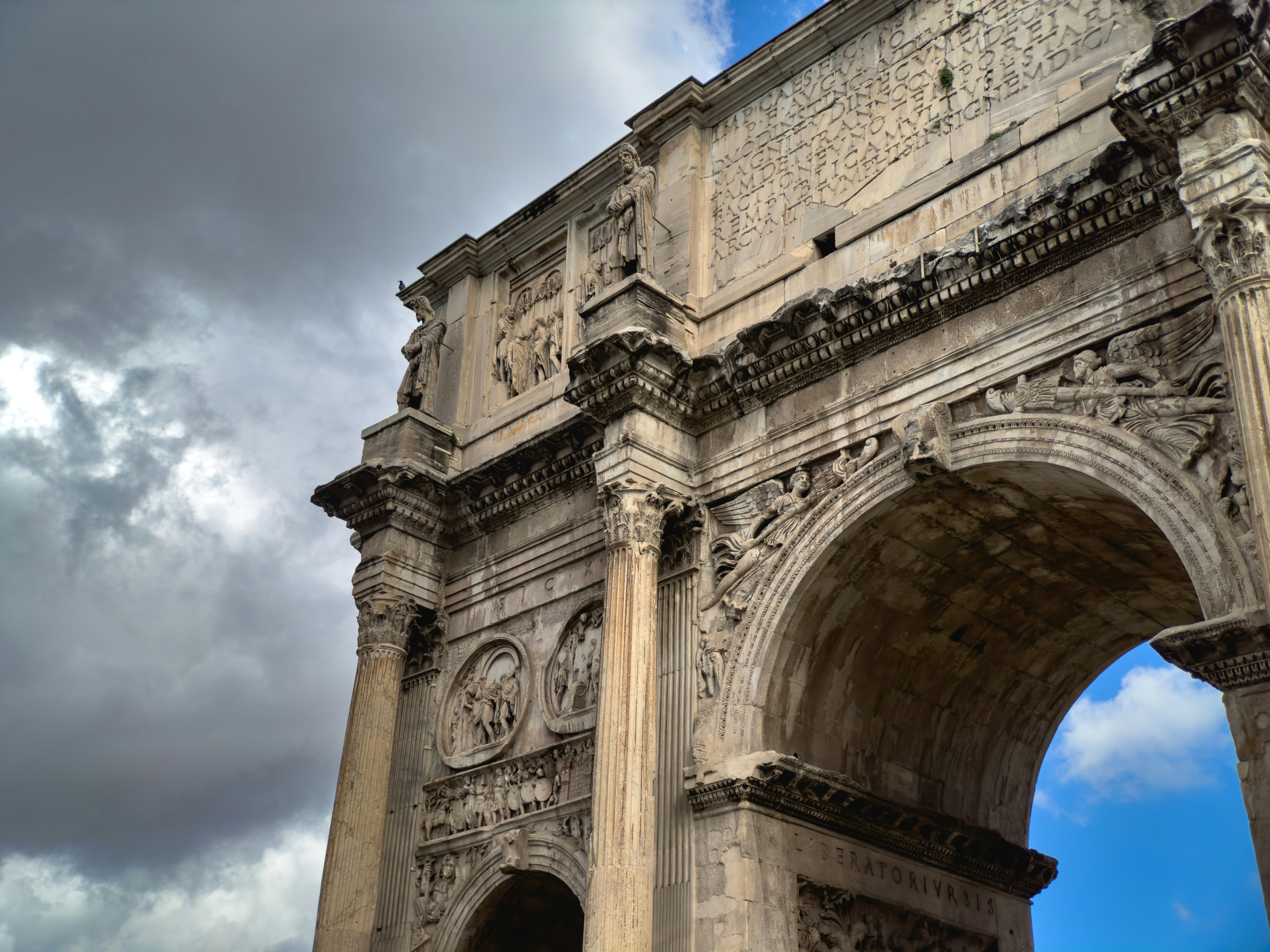 Ancient roman arch with intricate carvings against blue sky.