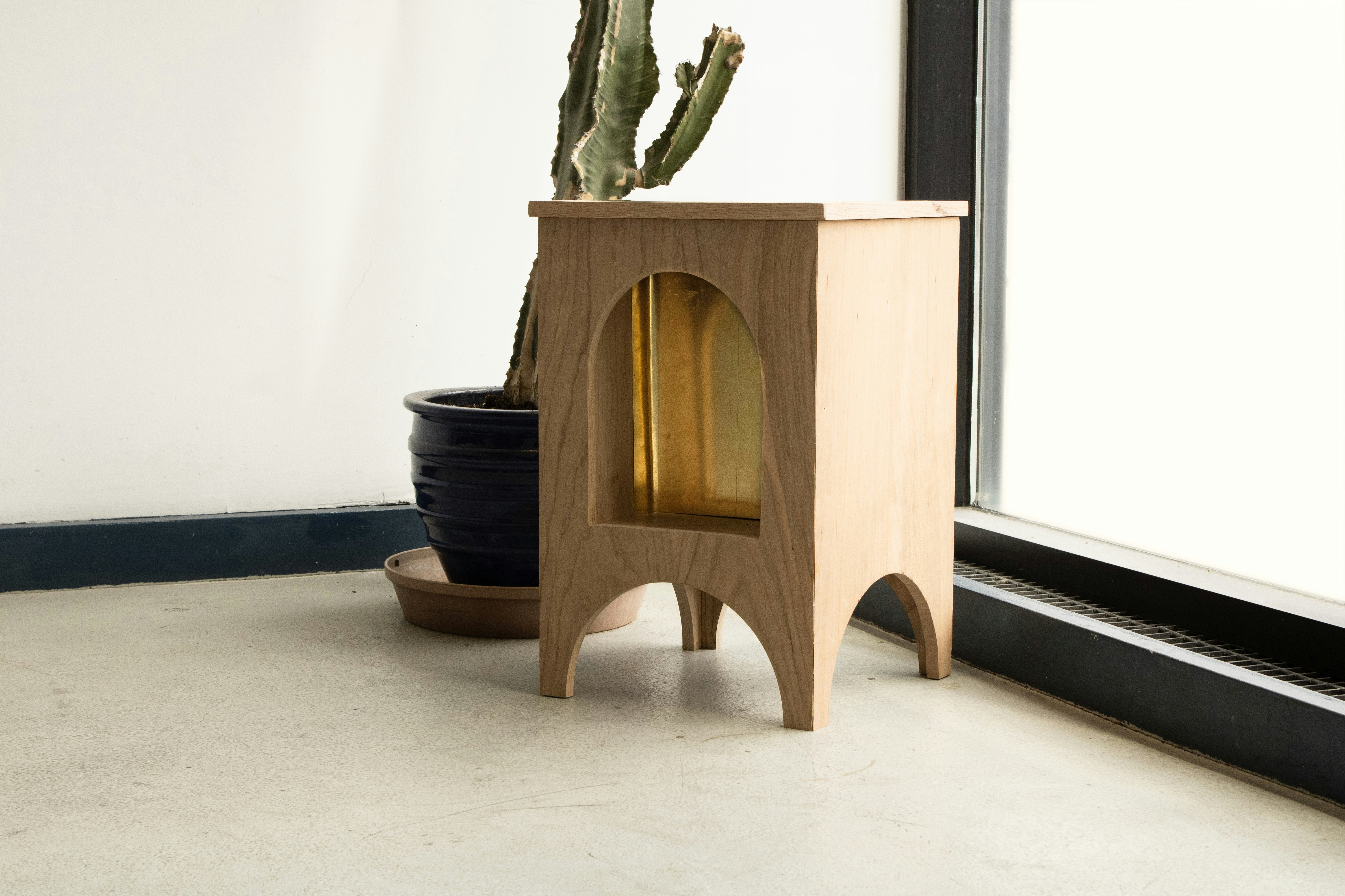 Wooden side table with arched cutout and plants.