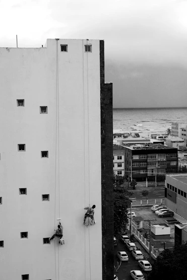Workers rappel down a building facade near the ocean