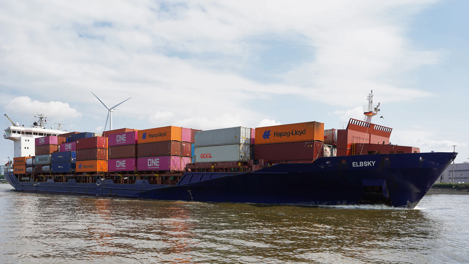 Large cargo ship loaded with containers sails on water.