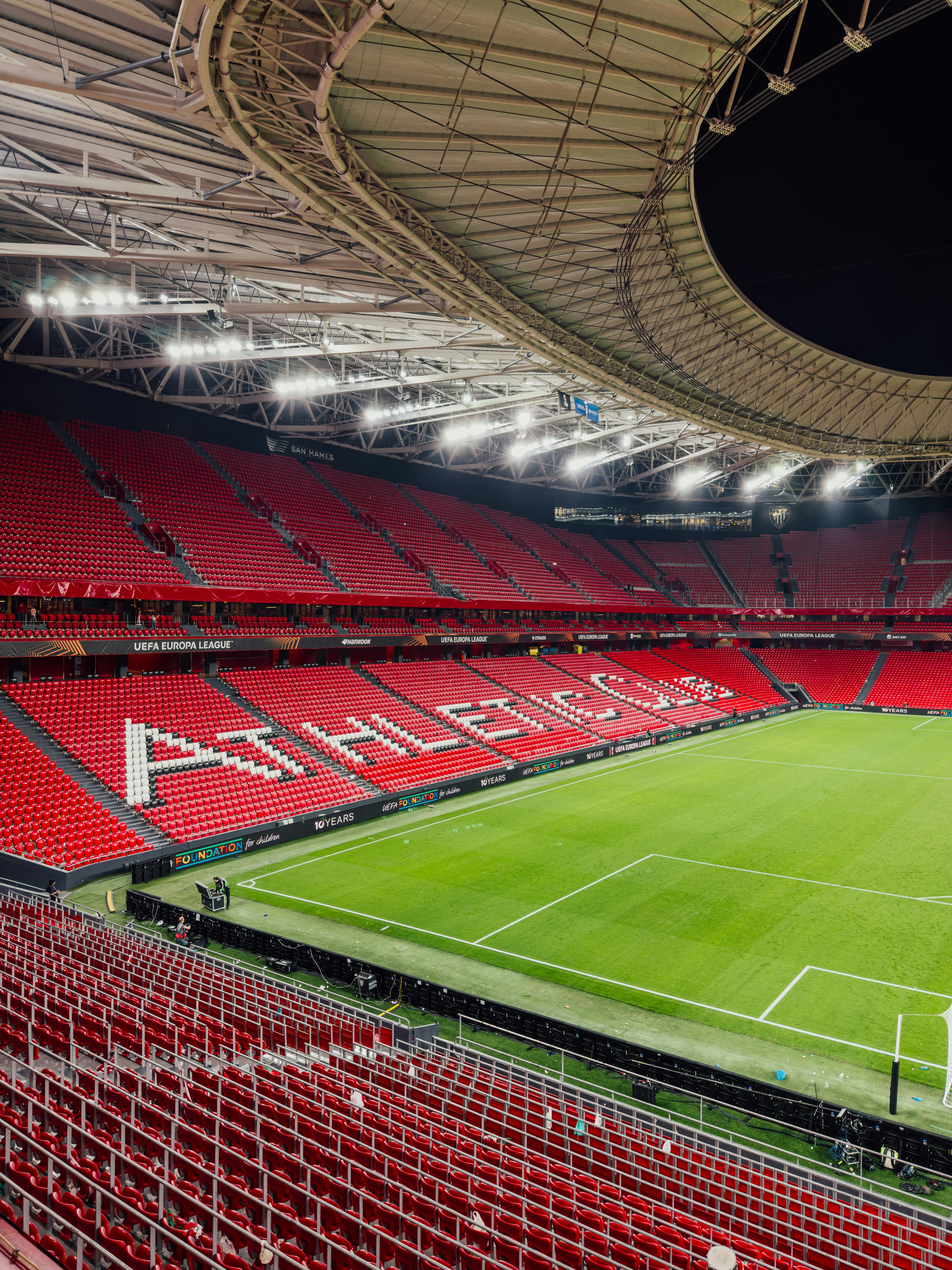 Empty stadium with red seats and green field.