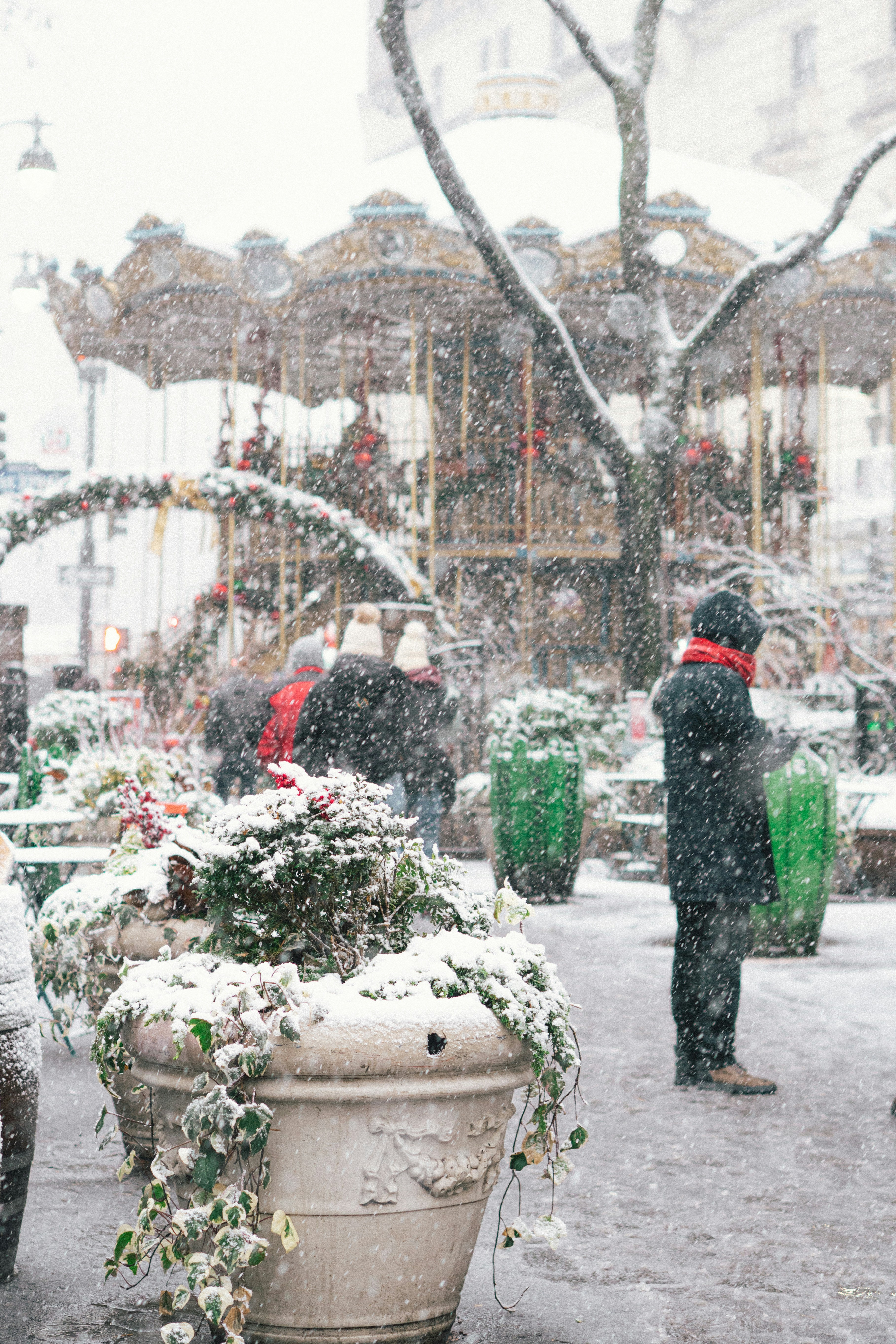 People walk past a carousel in the snow.