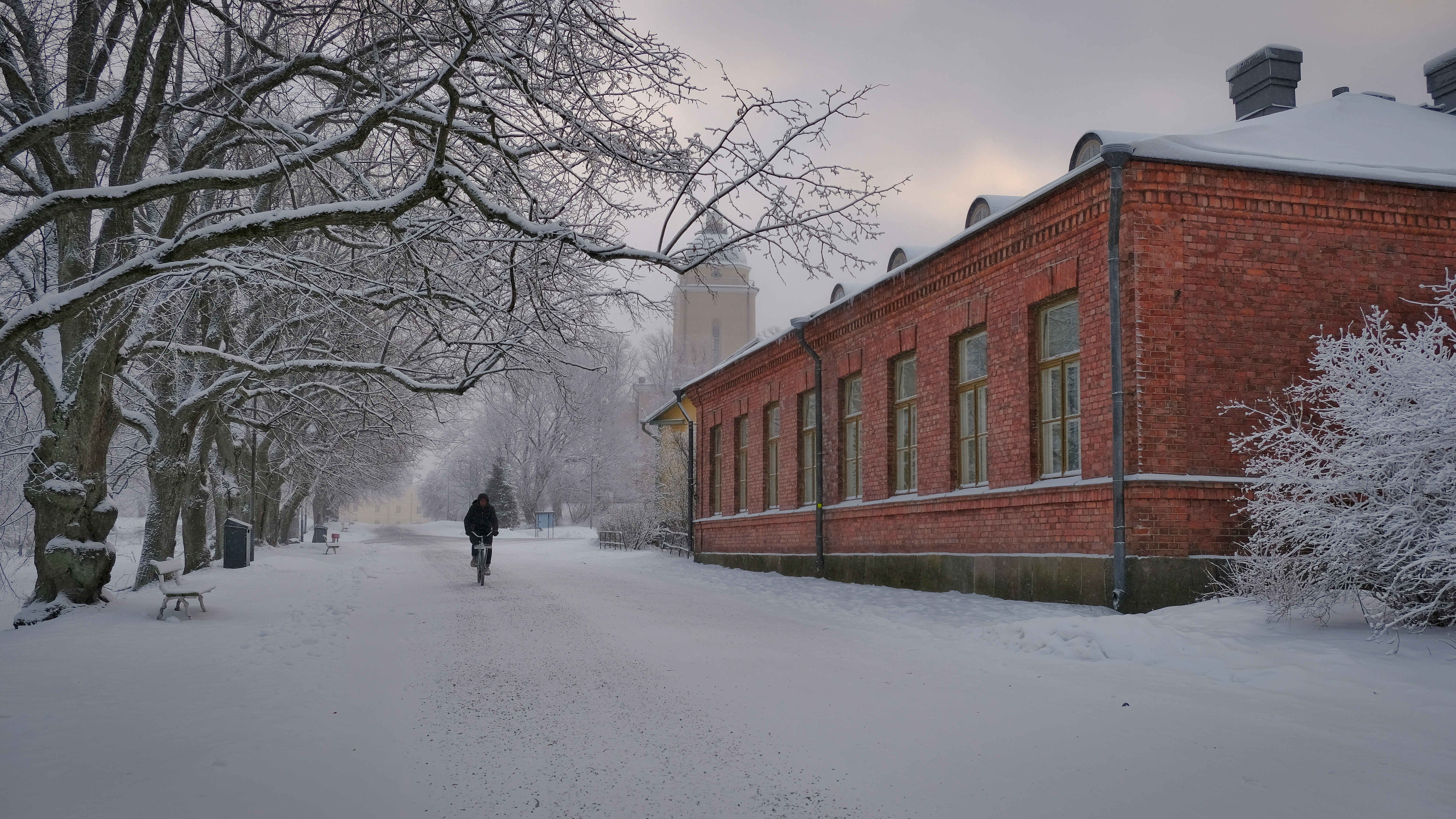 Person walking on snowy path beside brick building
