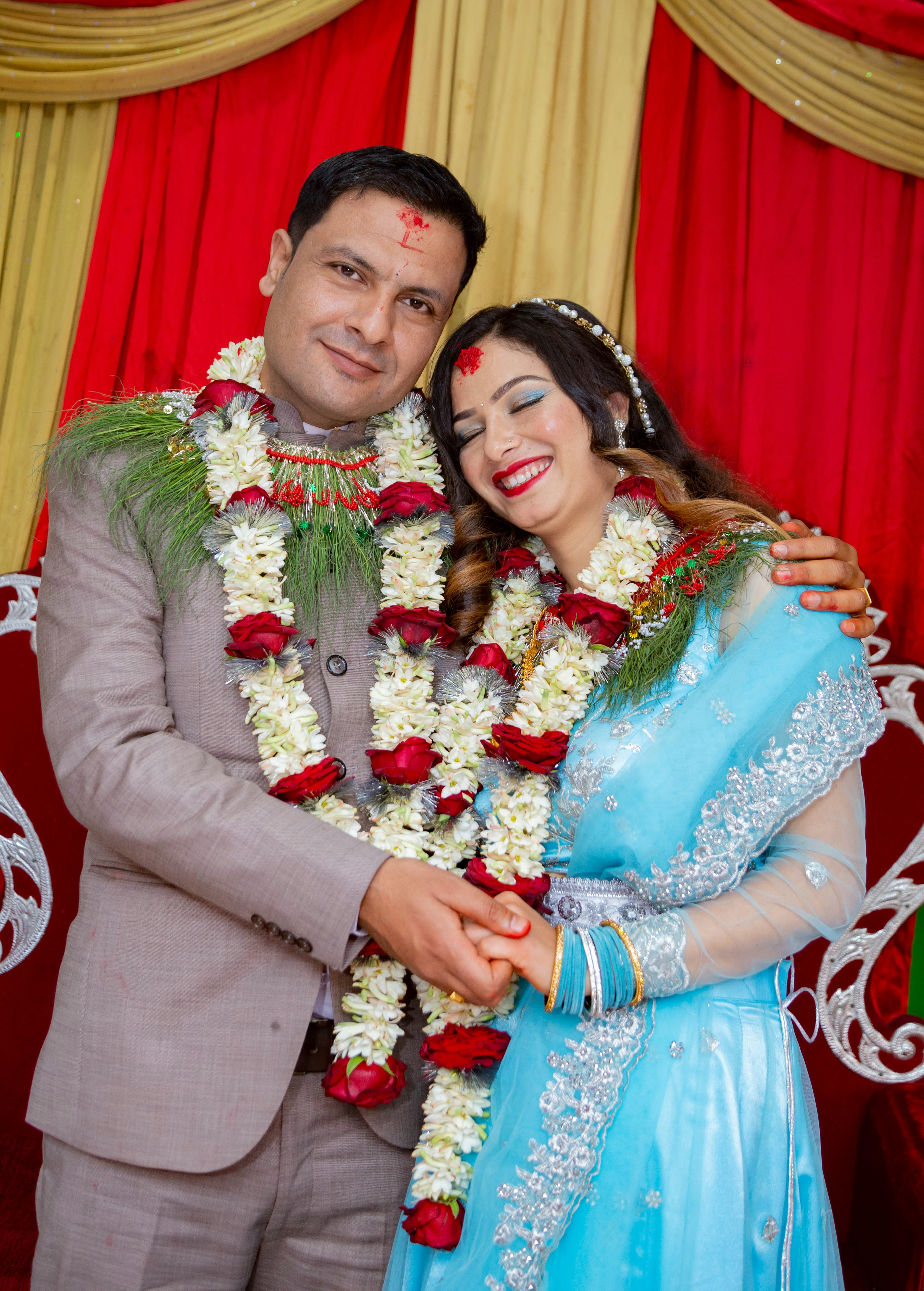 A smiling couple wearing garlands and traditional attire.