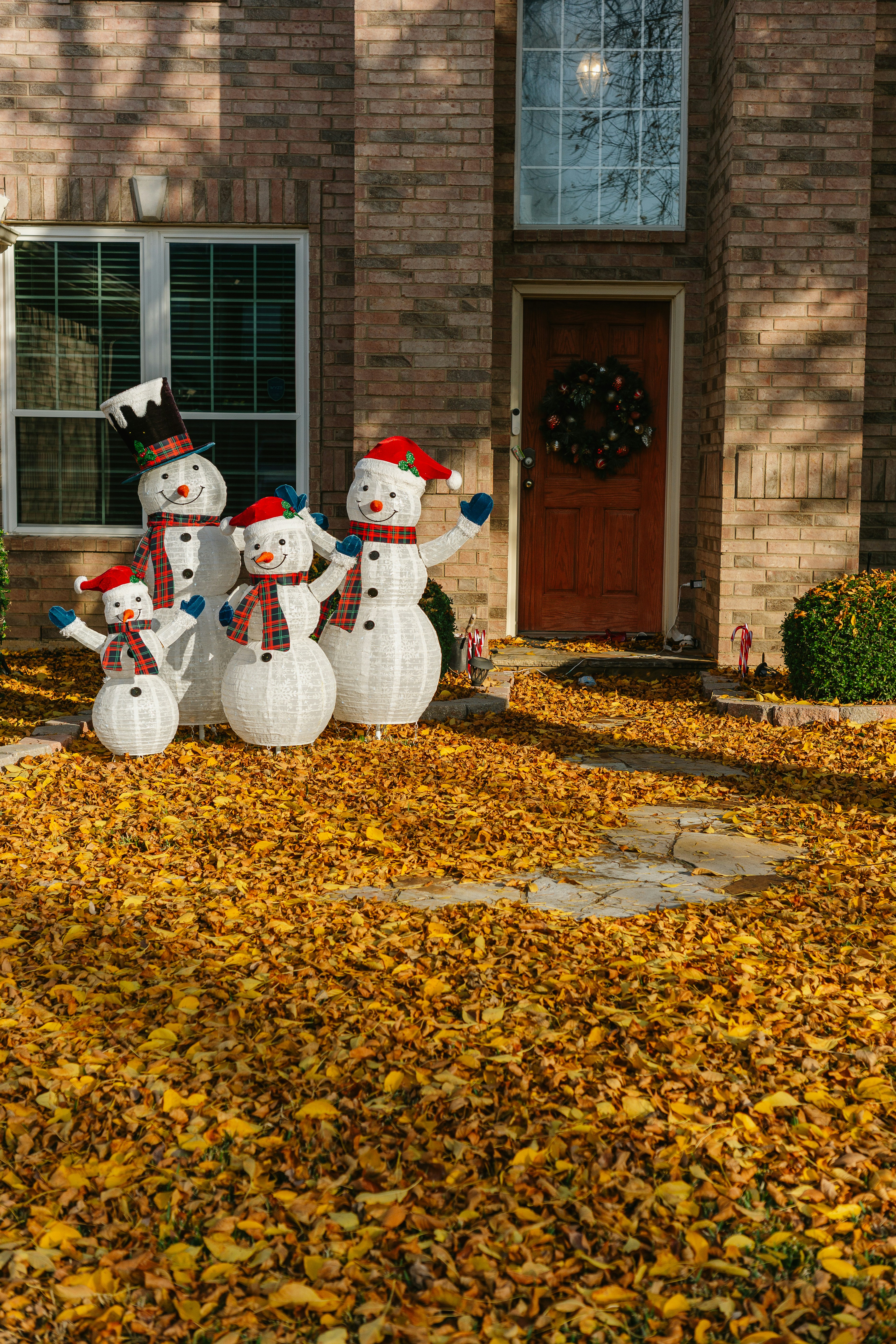 Snowman decorations on a lawn covered in autumn leaves.