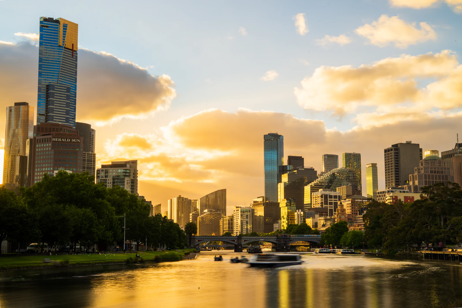 Melbourne skyline and the Yarra River at golden hour with a boat passing under a bridge, a city where an Australia eSIM handles trams and maps
