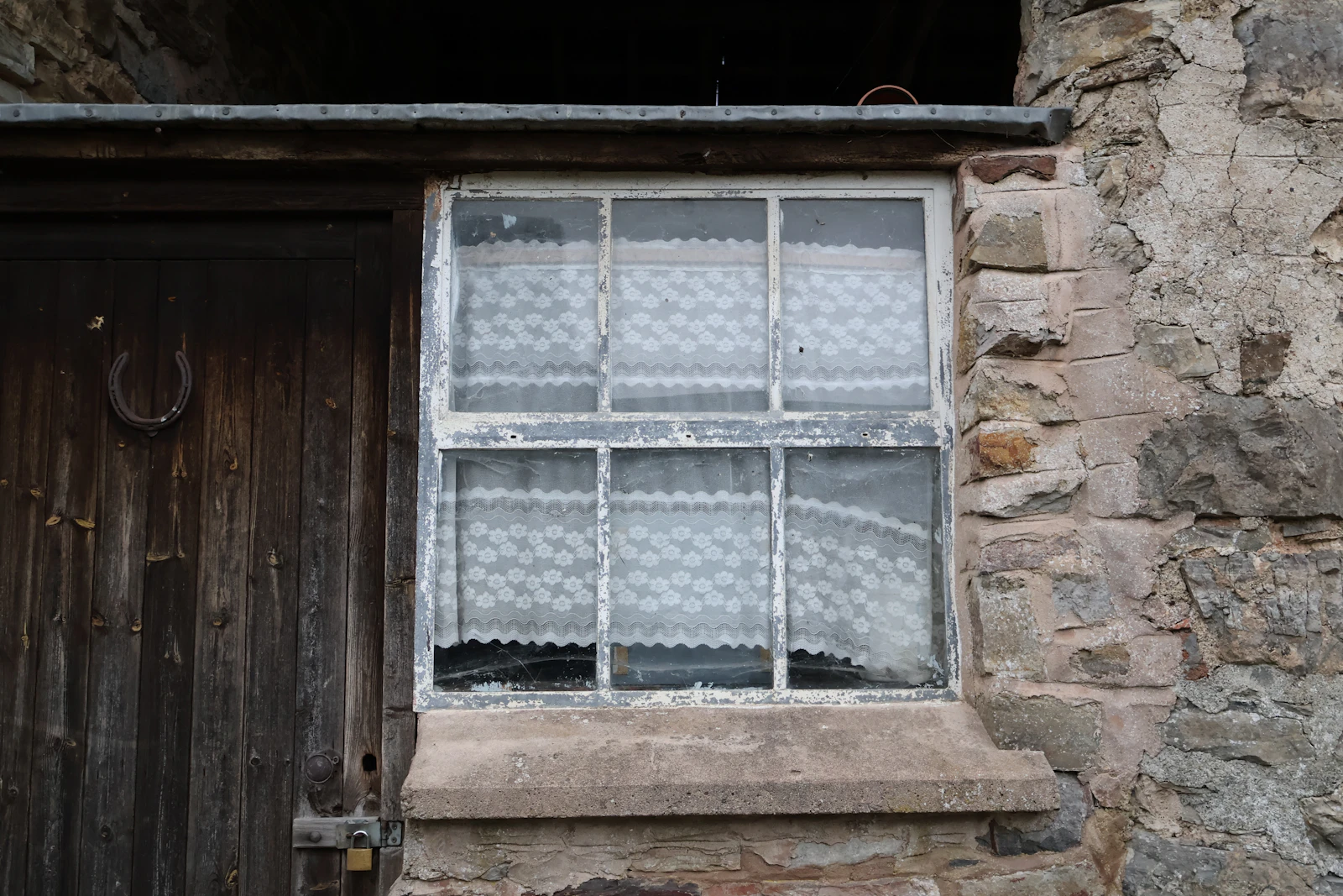 Old window with lace curtains beside a weathered door