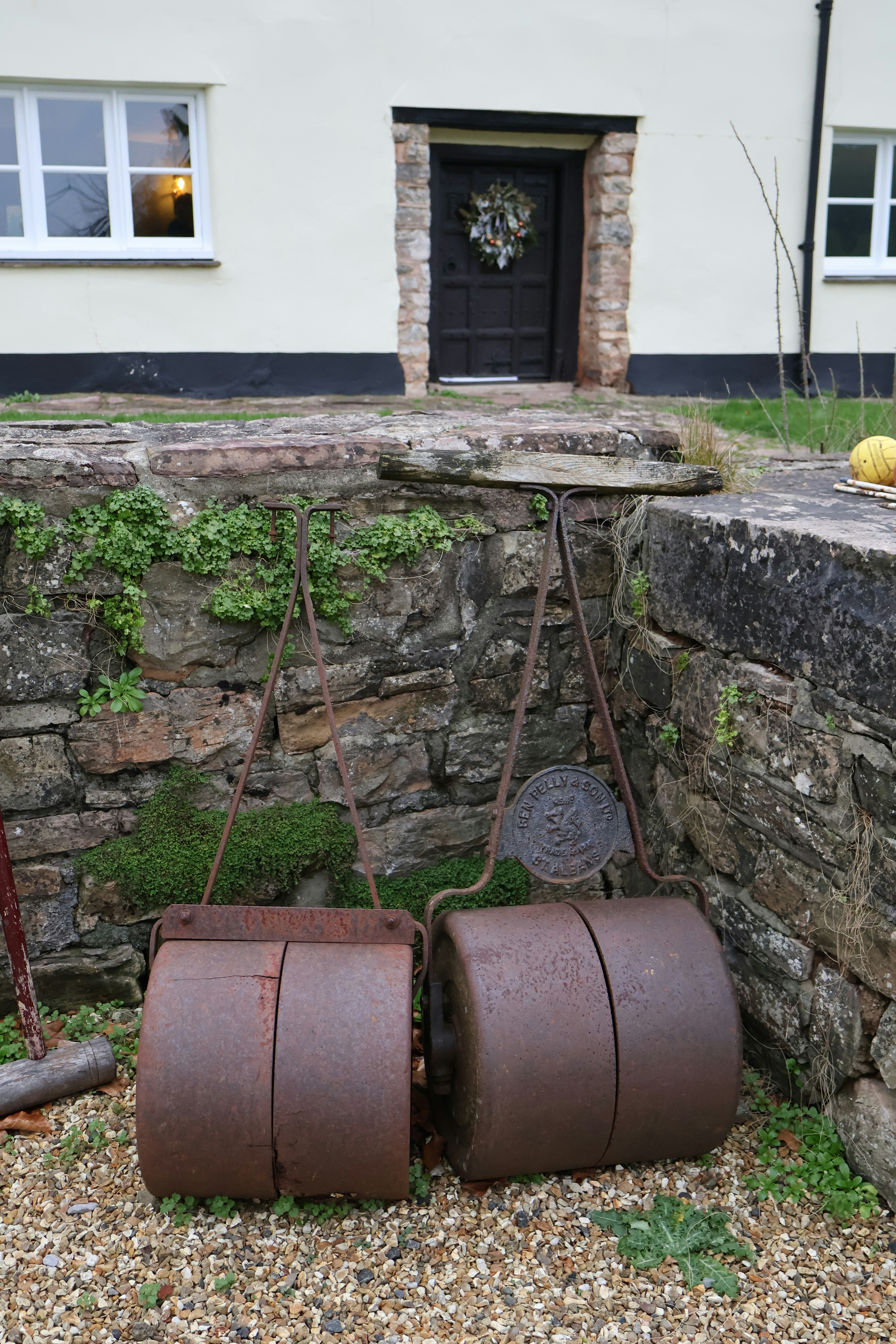 Two rusty antique lawn rollers rest outside.