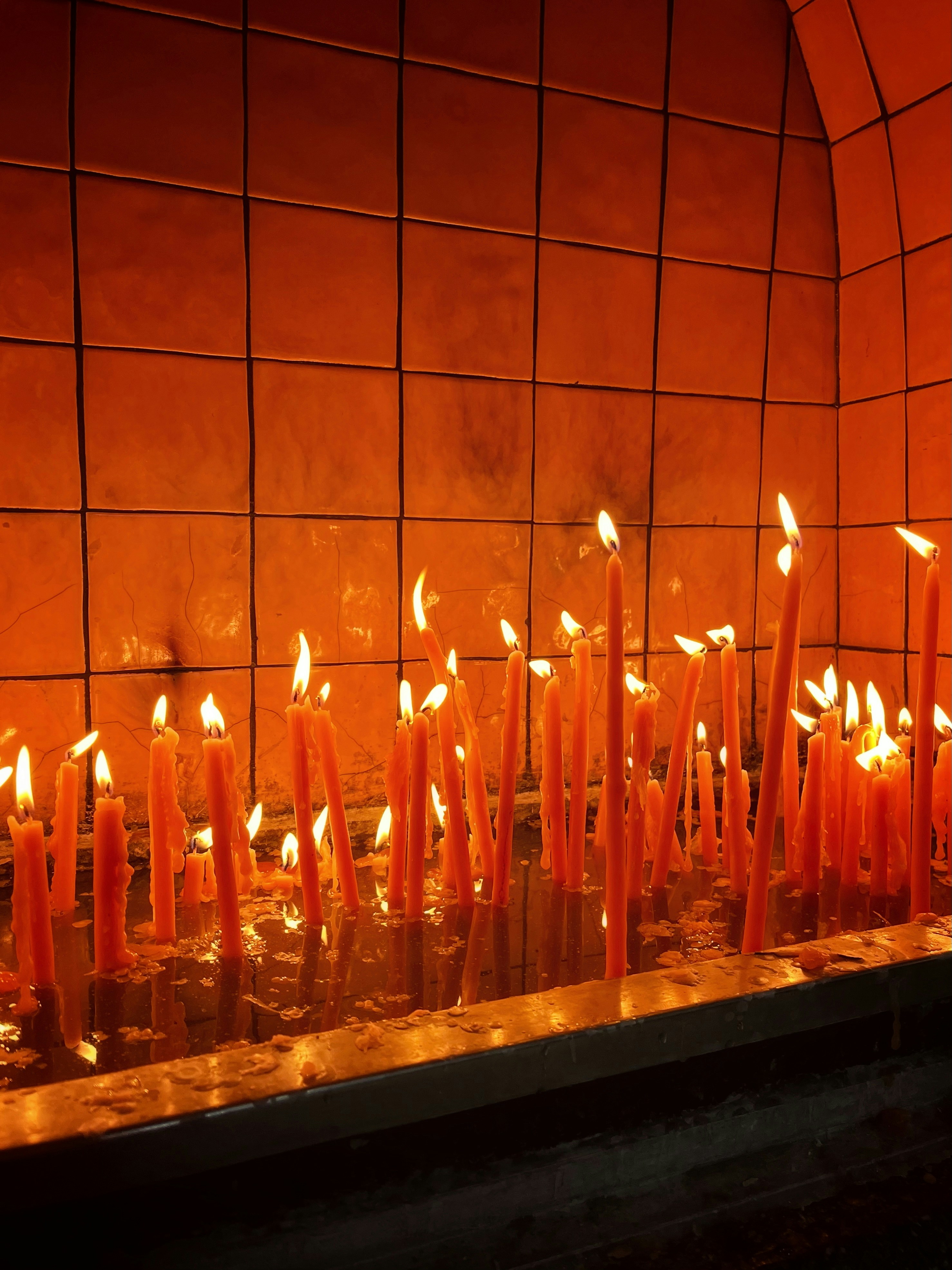 多くの人がタイル張りの祠でオレンジ色のろうそくに火を灯しました