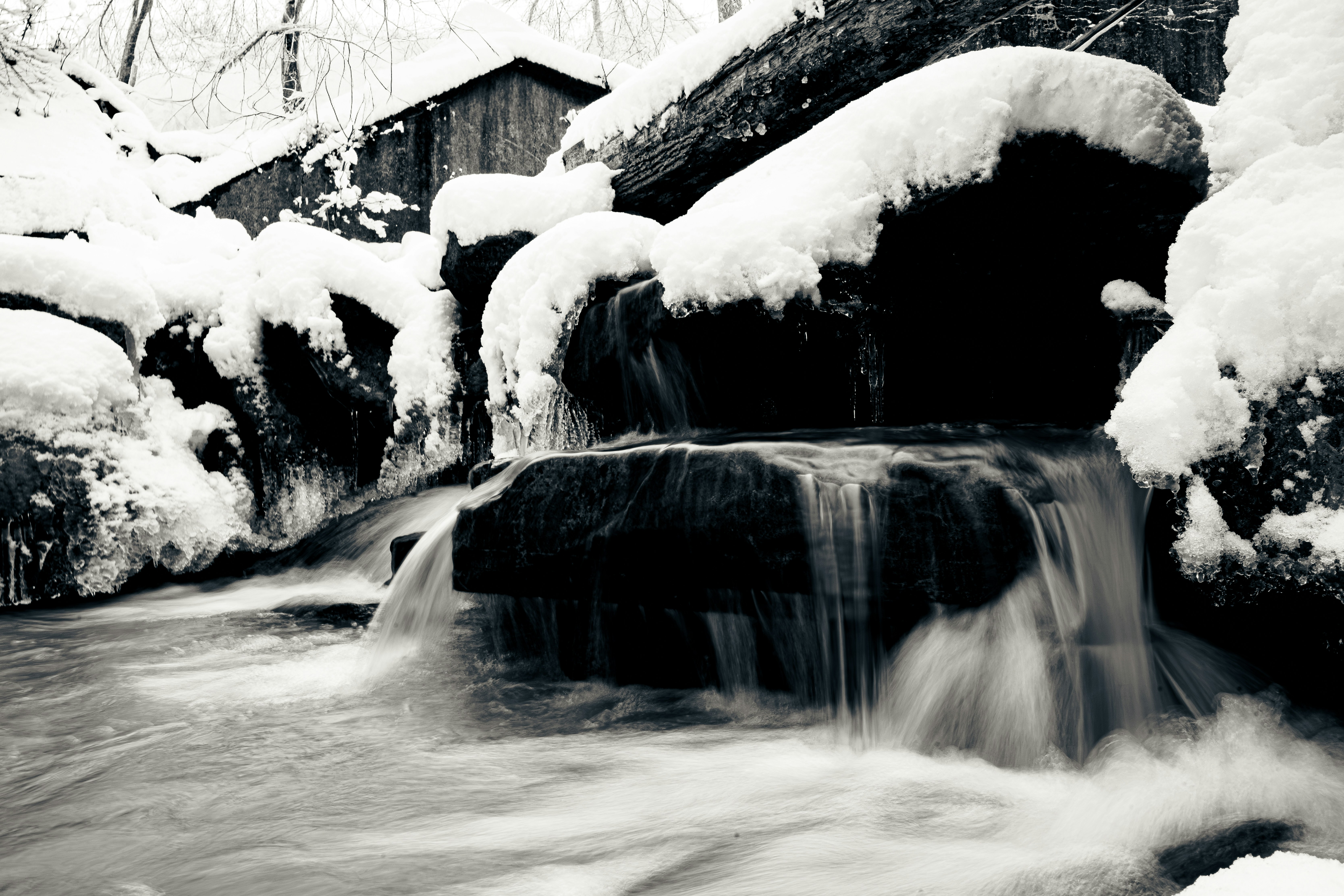 A small waterfall flows over rocks covered in snow.