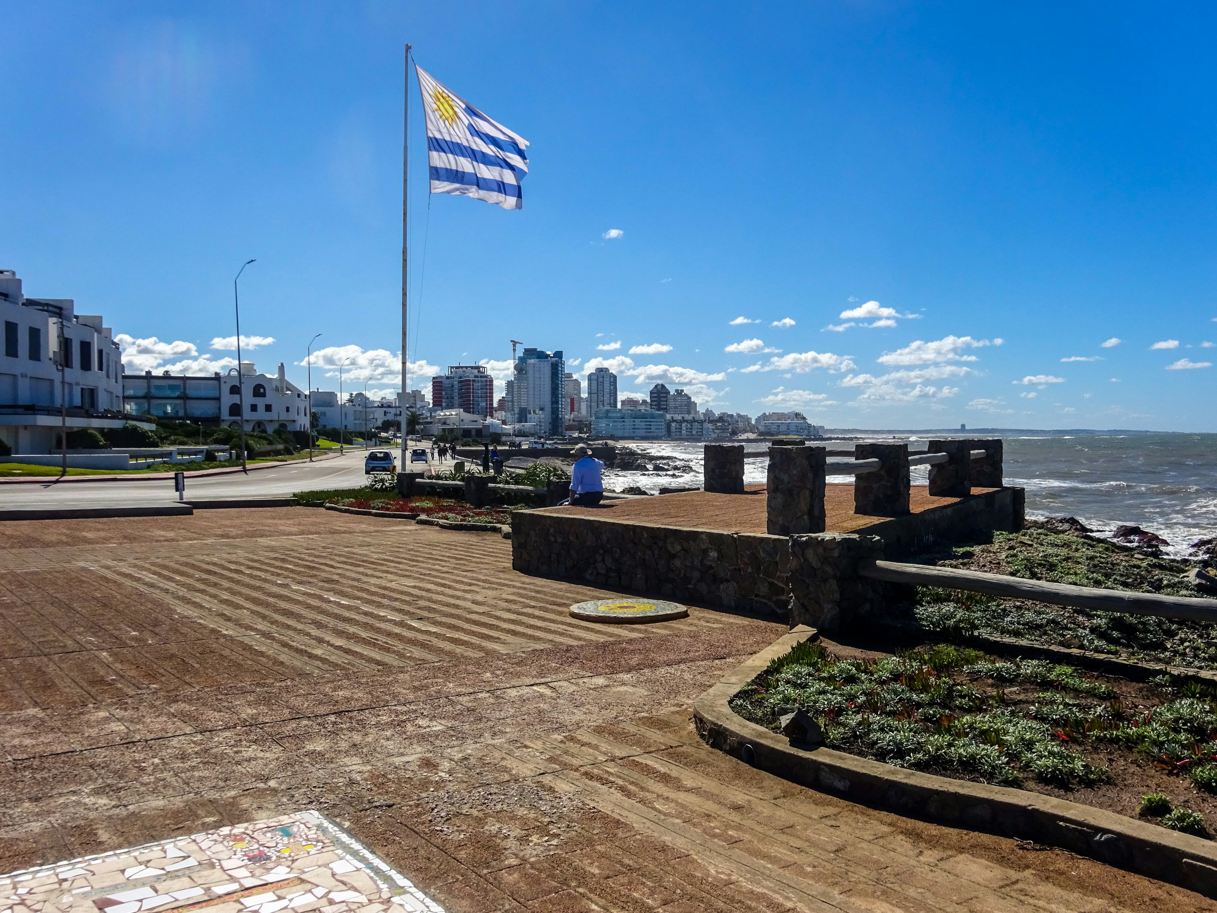 Uruguayan flag flies over a coastal city skyline.