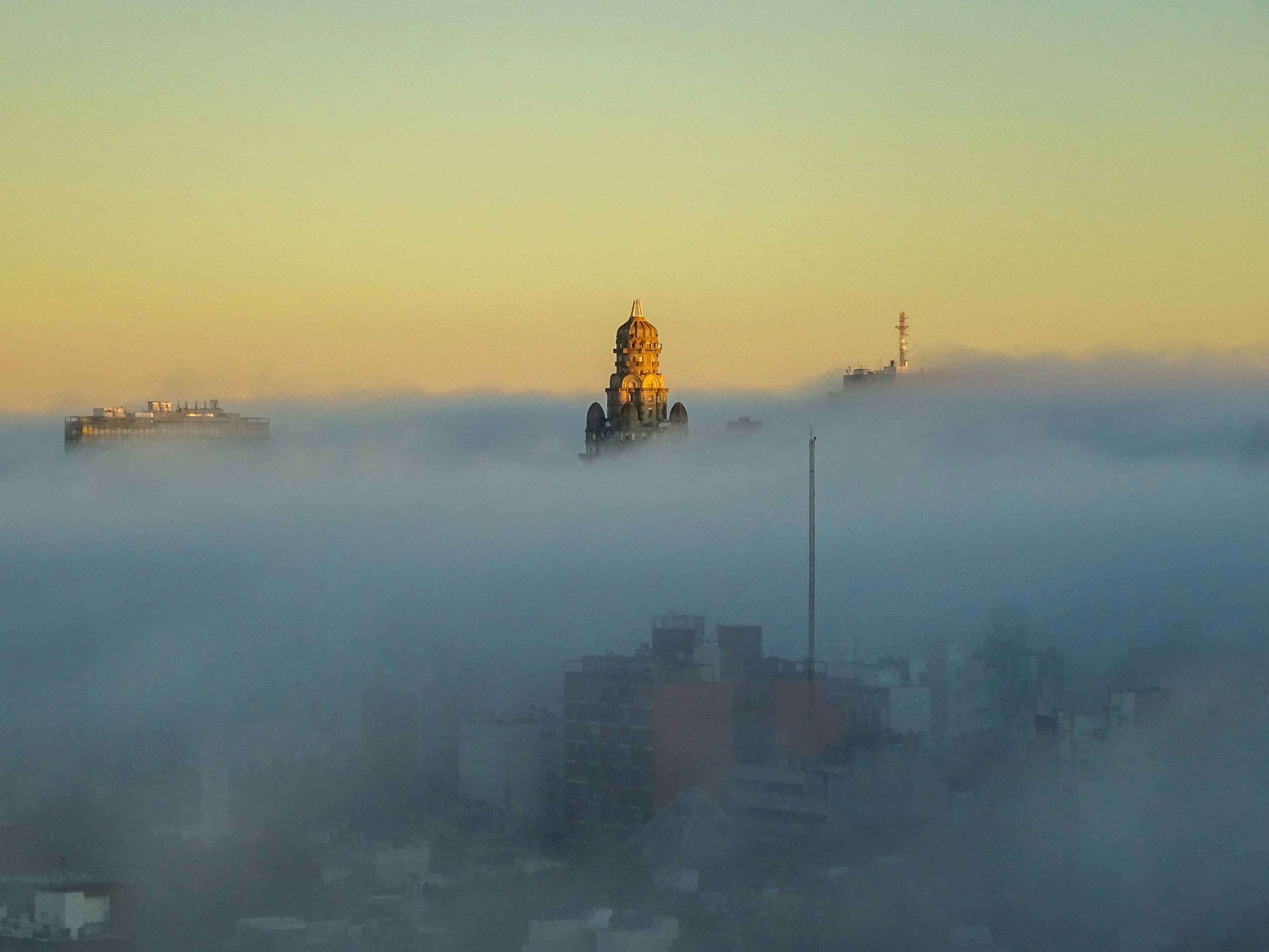 Buildings emerge from thick fog at sunrise.