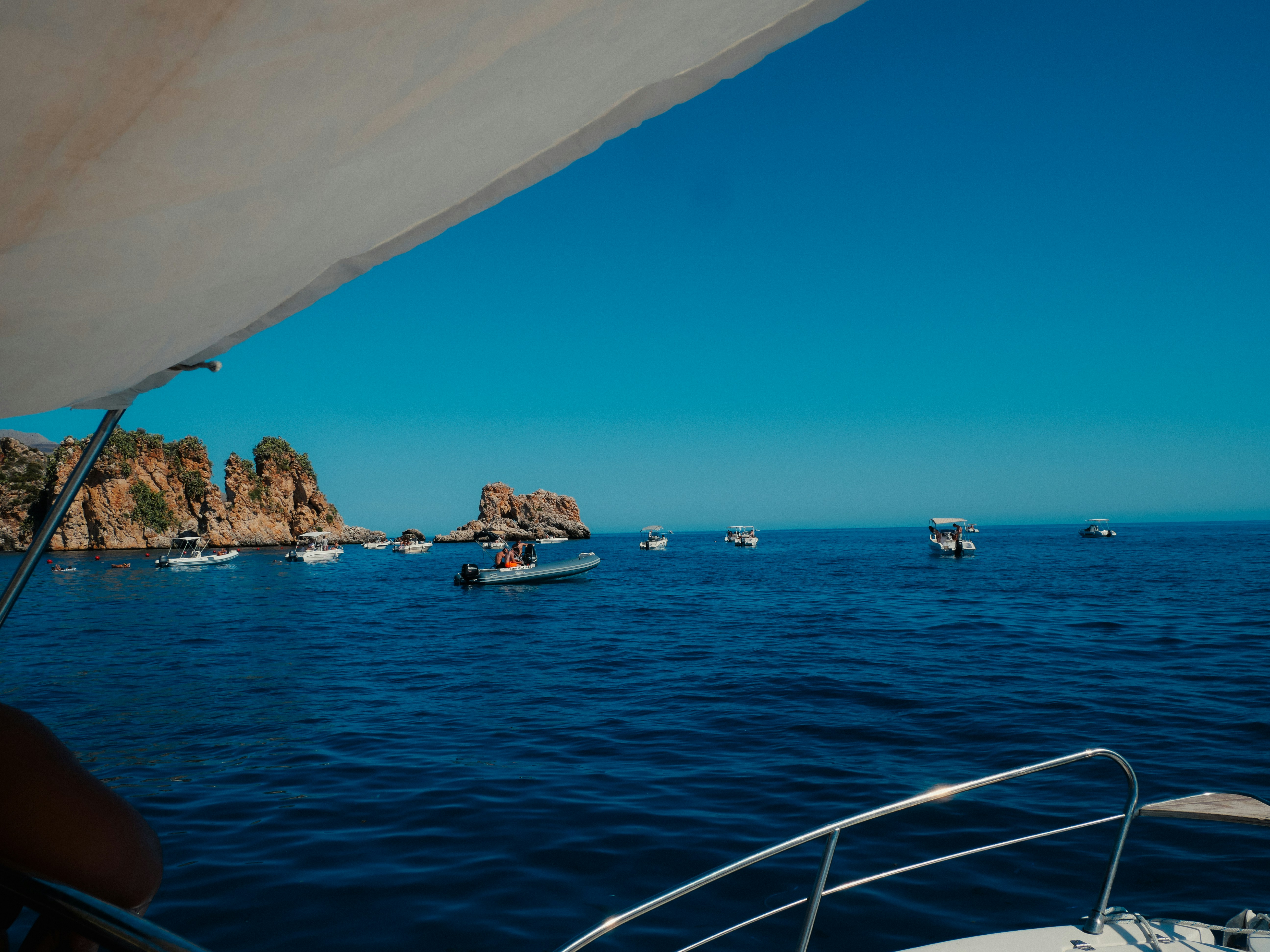 Boats anchored in a calm blue ocean near rocky islands.