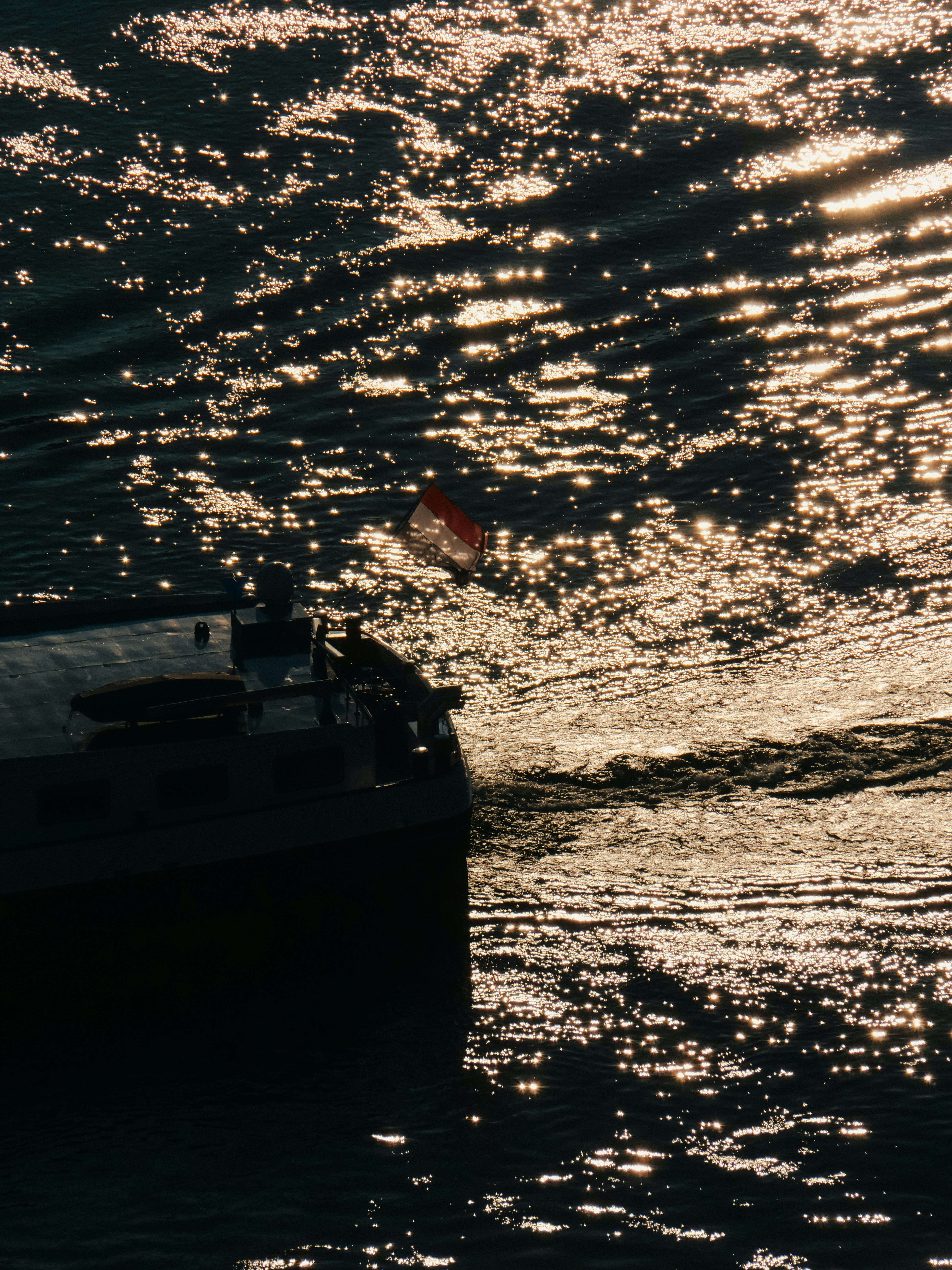 A ship sails on shimmering water at sunset.