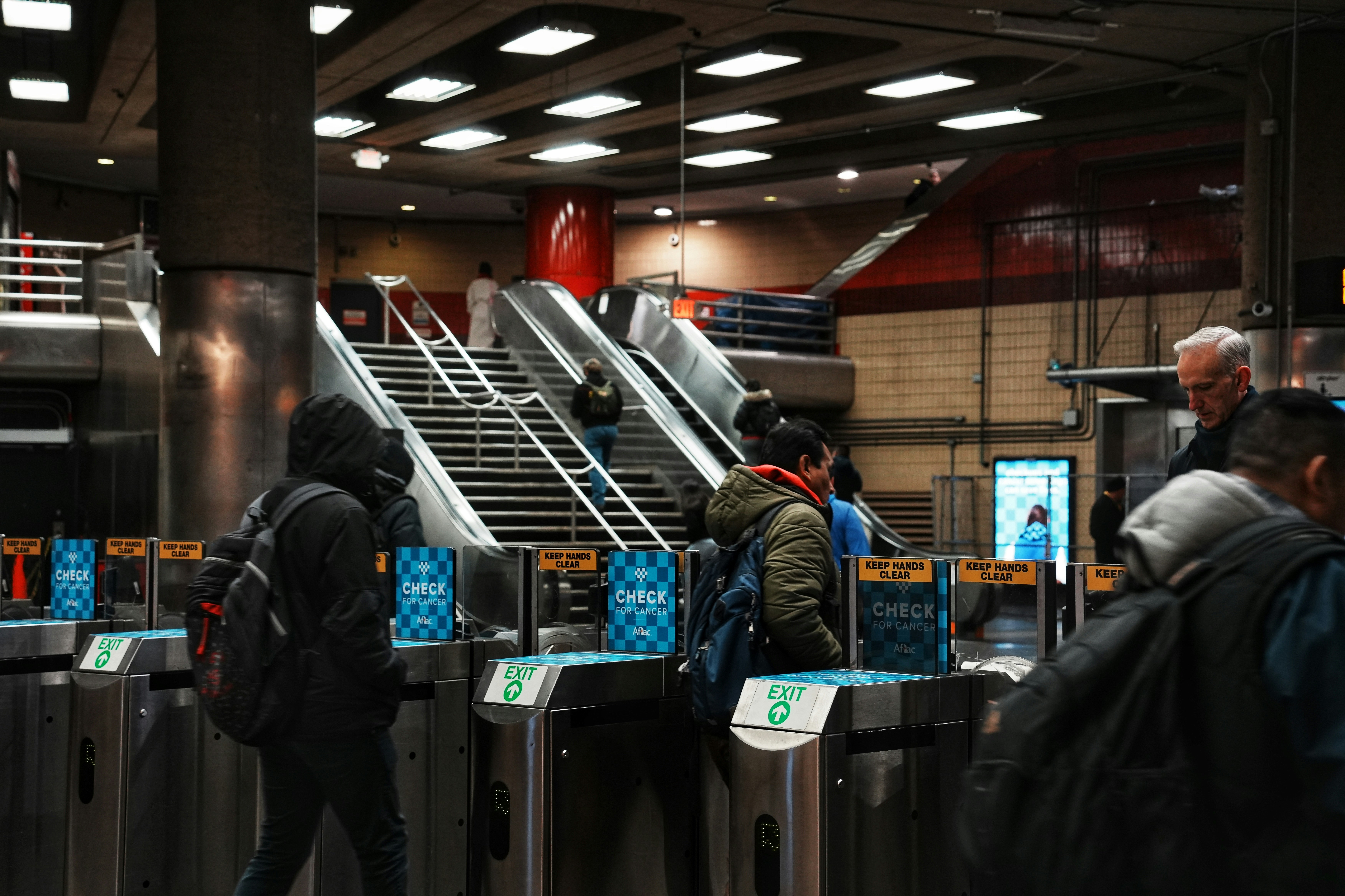 People entering subway turnstiles with escalators behind them.