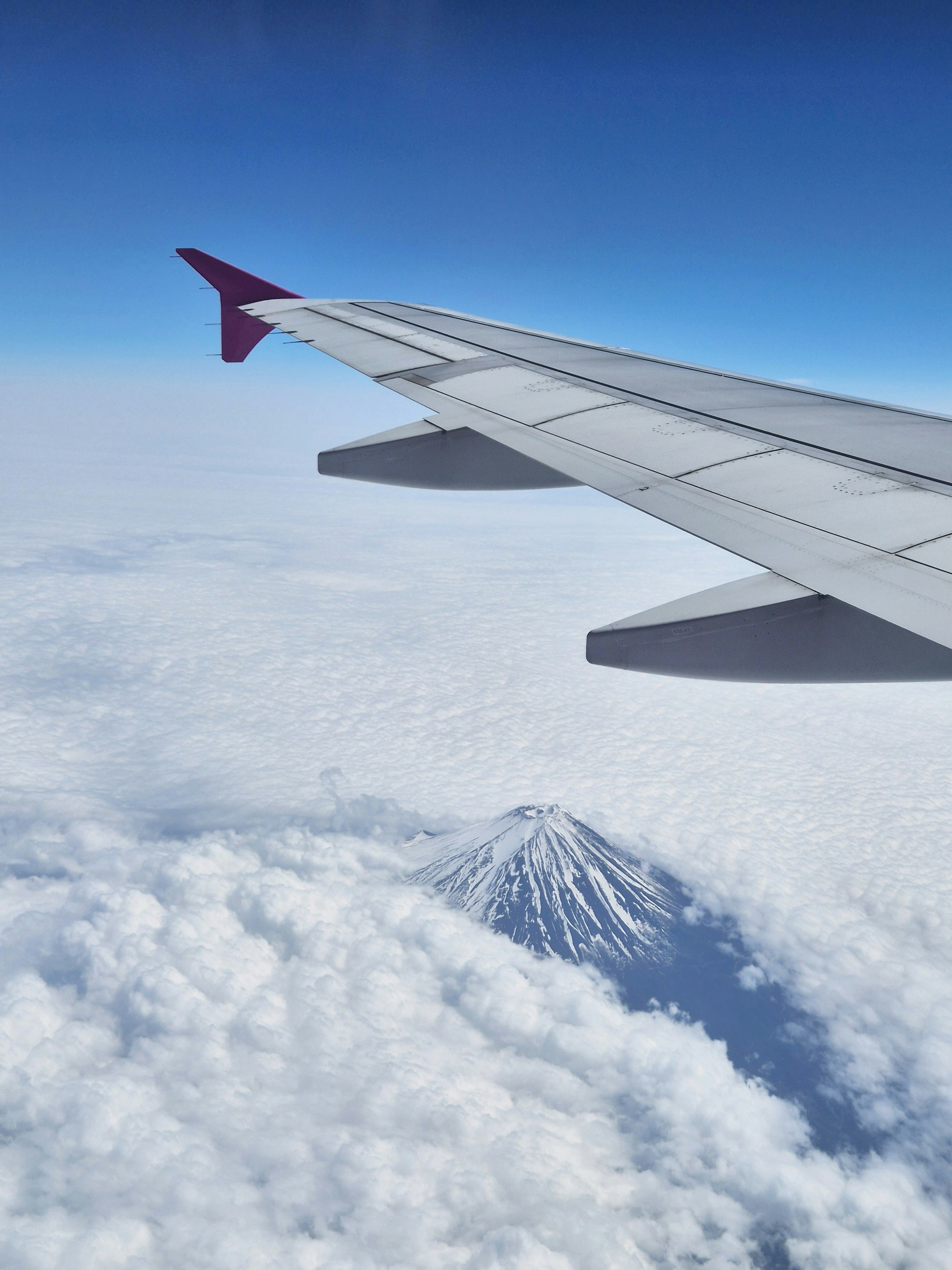 Airplane wing over snow-capped mountain above clouds.