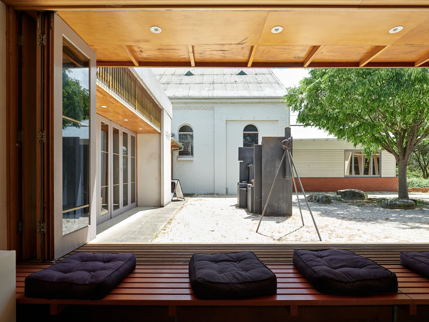 A gravel courtyard with one tree between two low painted wings