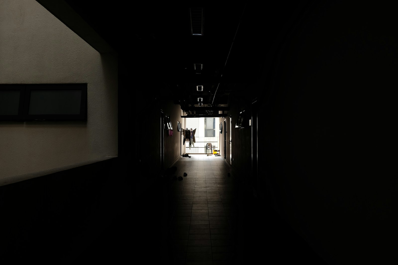 A dark hallway stretching toward a luminous exit, evoking the tension between solitary independence and the pull of a larger institution