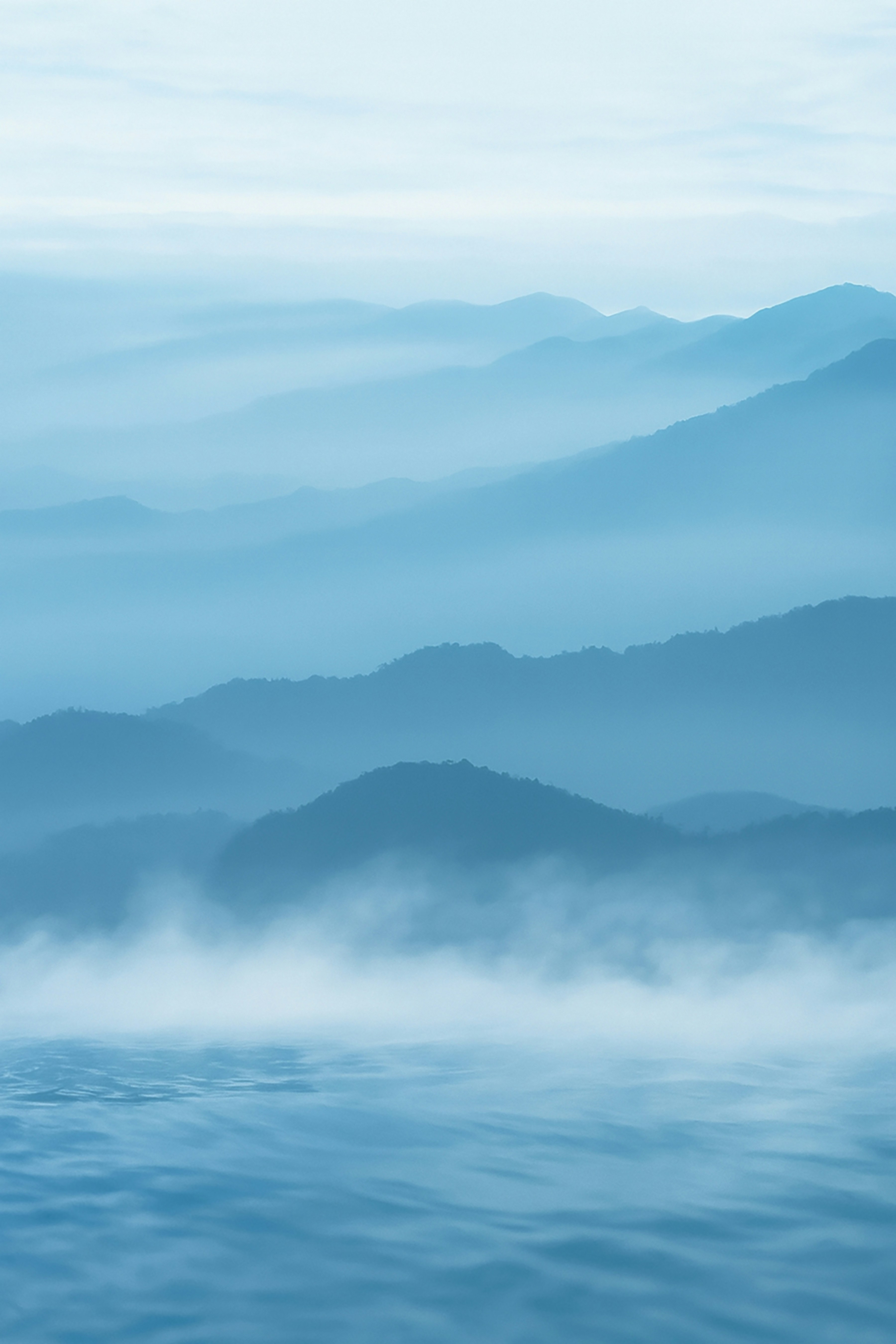 Misty blue mountains rise above calm water.