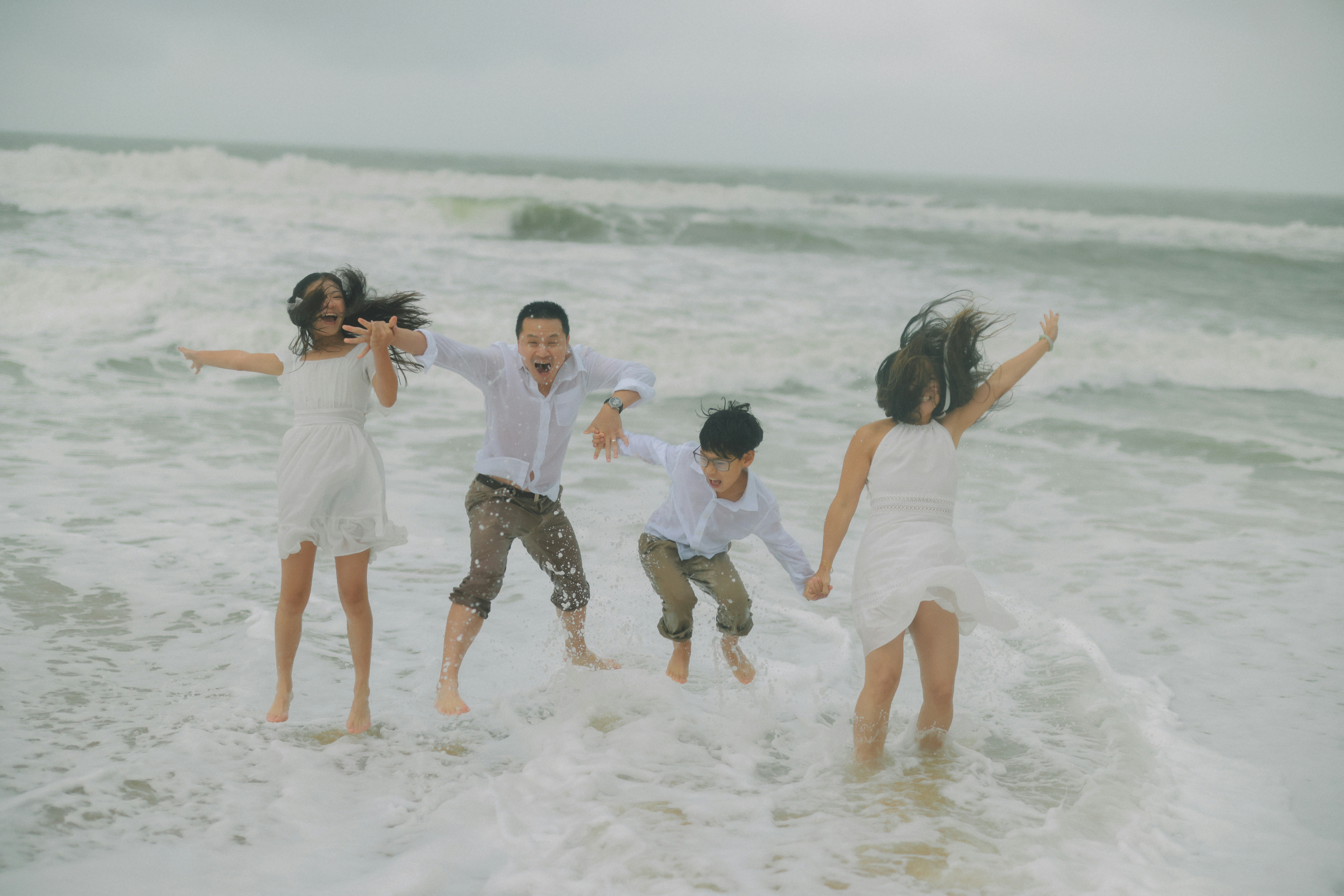 Family jumping in ocean waves on a cloudy day