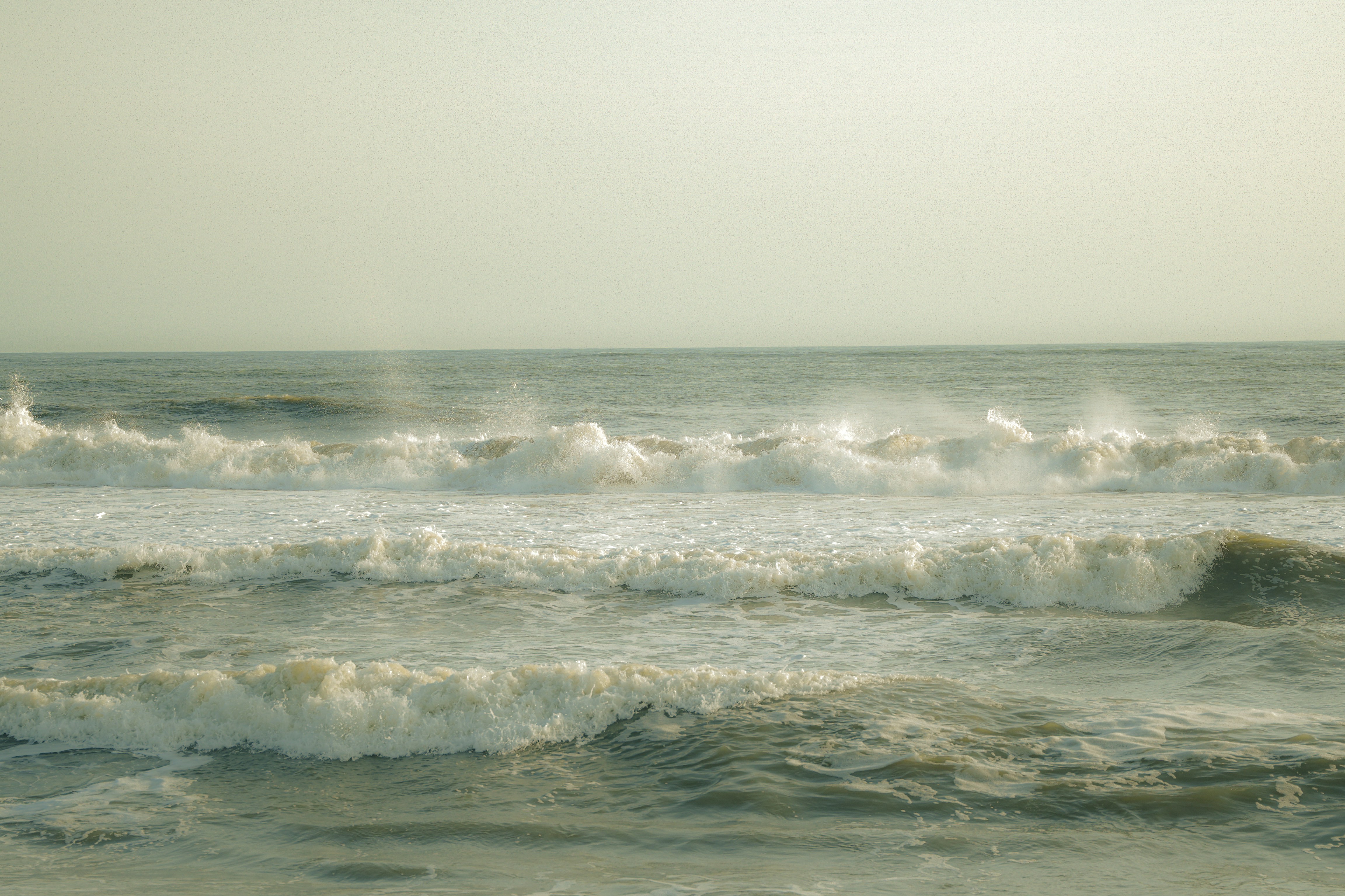 Waves crash on a sandy beach under a hazy sky.