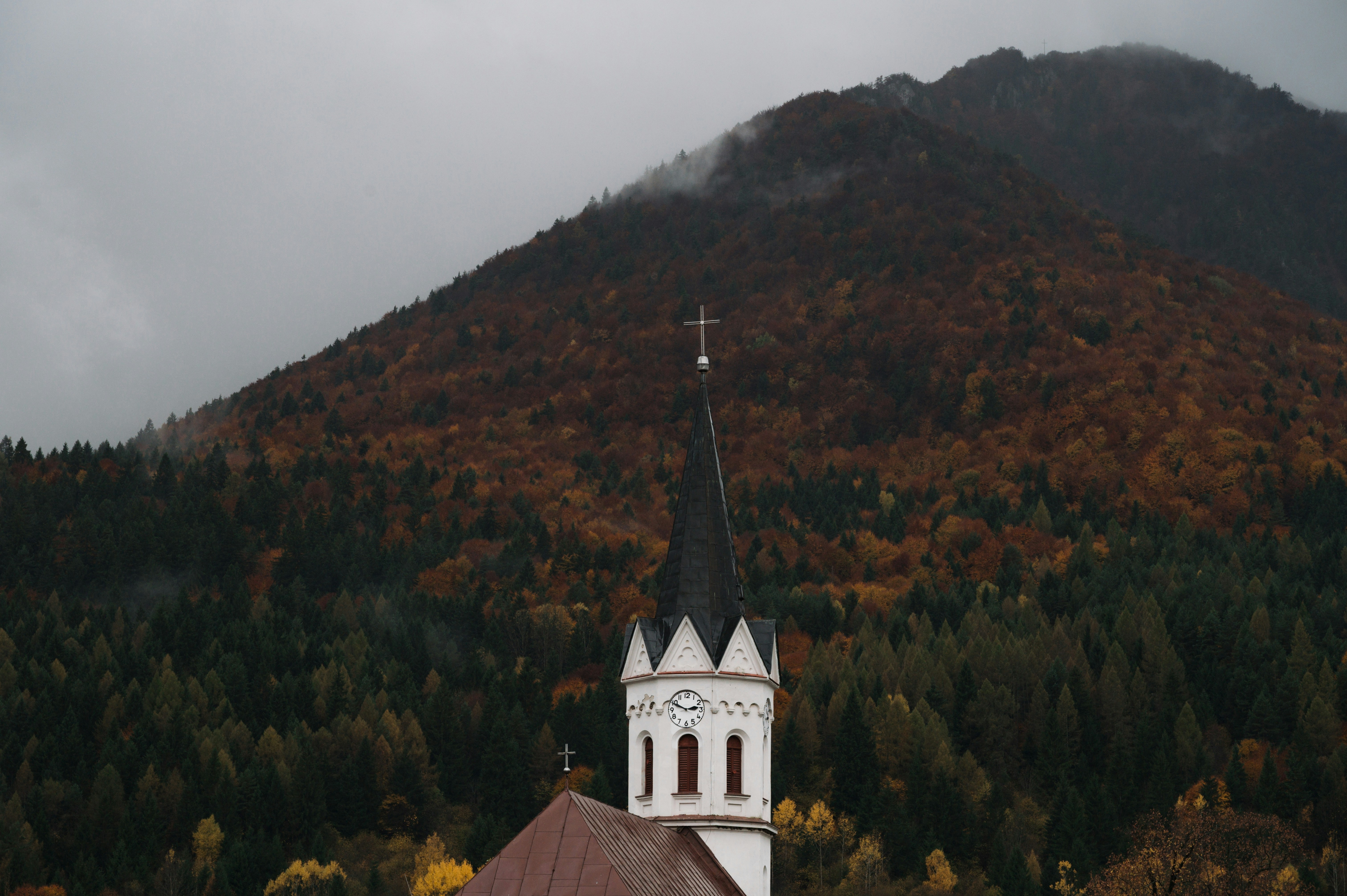 Church steeple against a mountain and autumn forest.