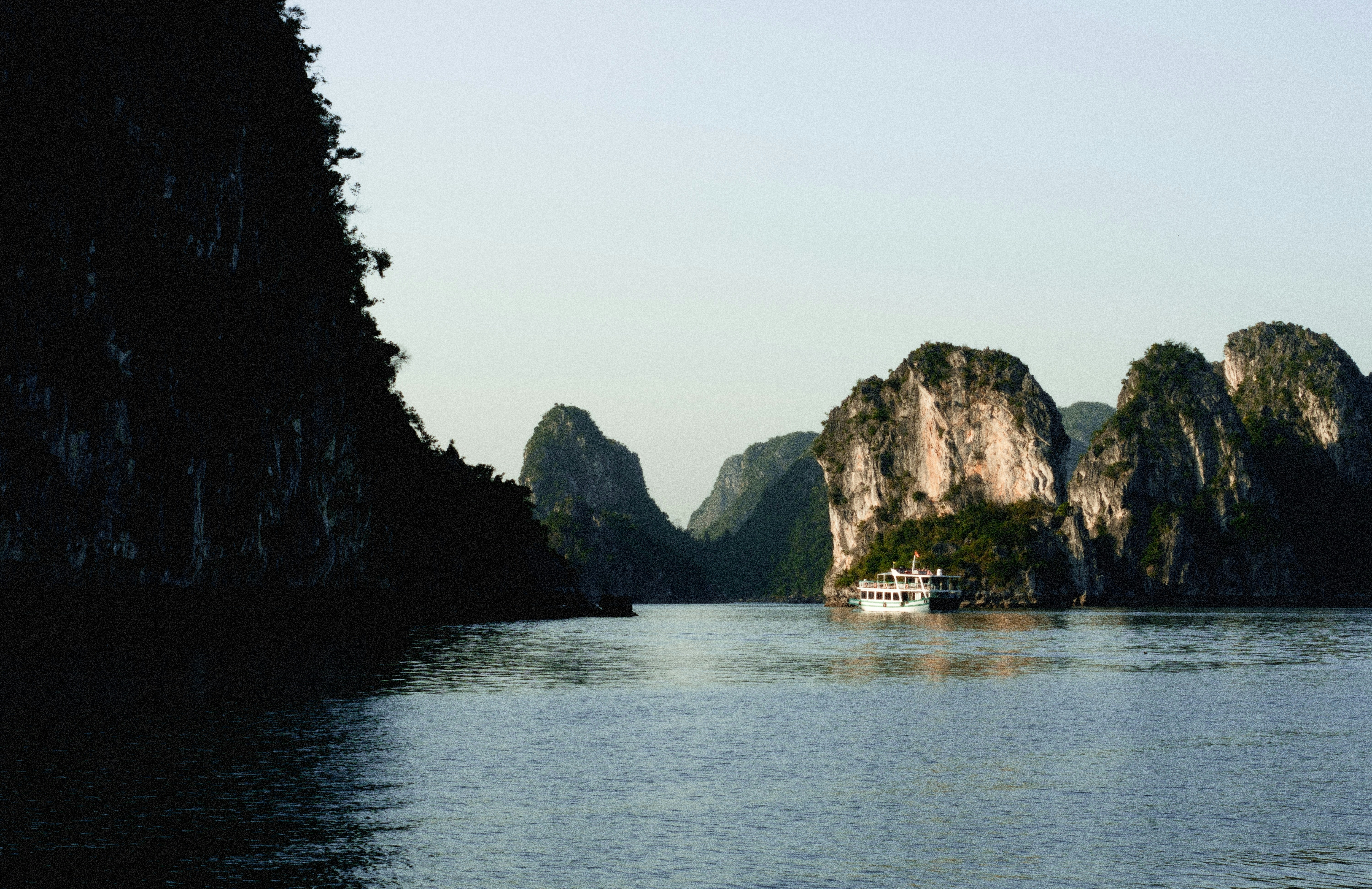 Limestone karsts rise from the water with a boat.