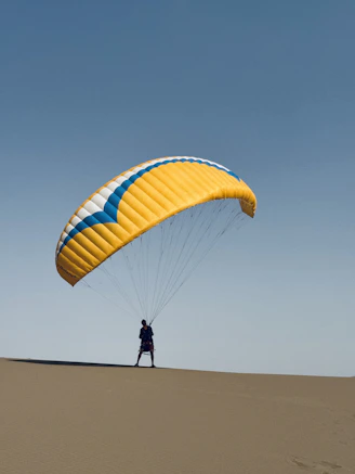 Man with paraglider on sand dune against blue sky